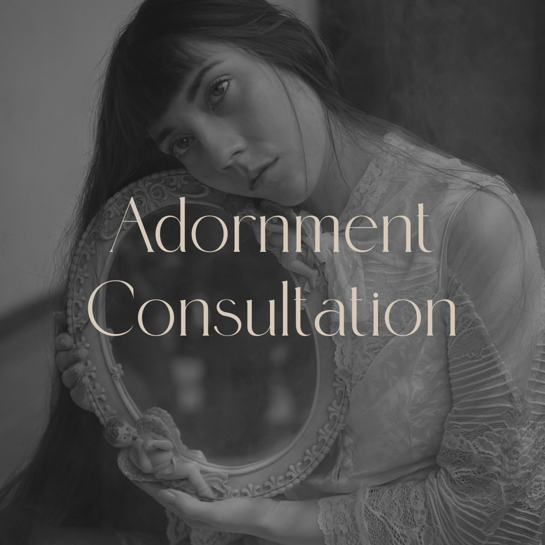 A young woman with long hair looking into a mirror she holds, with the words "Adornment Consultation" overlaid.