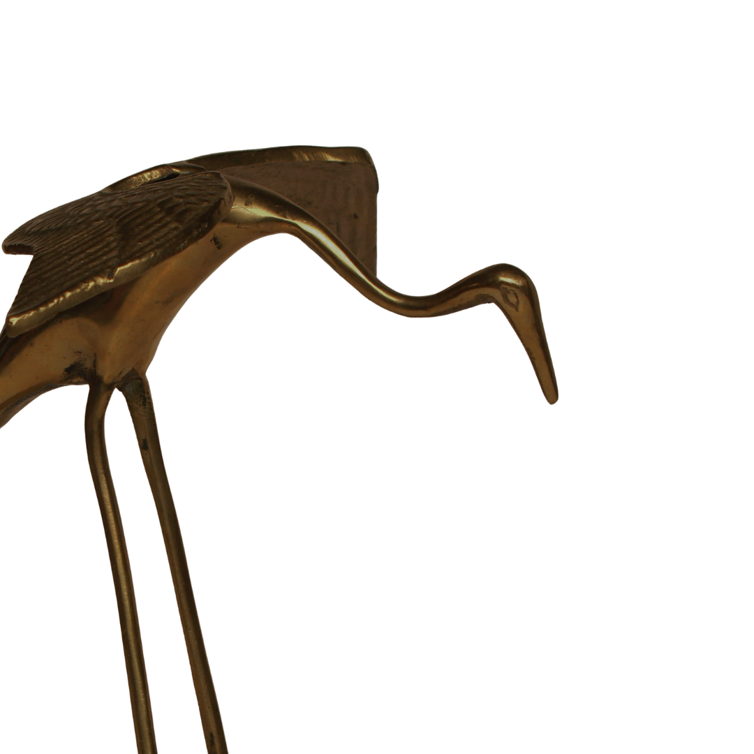 Close-up of a metallic bird sculpture with elongated, curved beak and textured wings against a plain background.