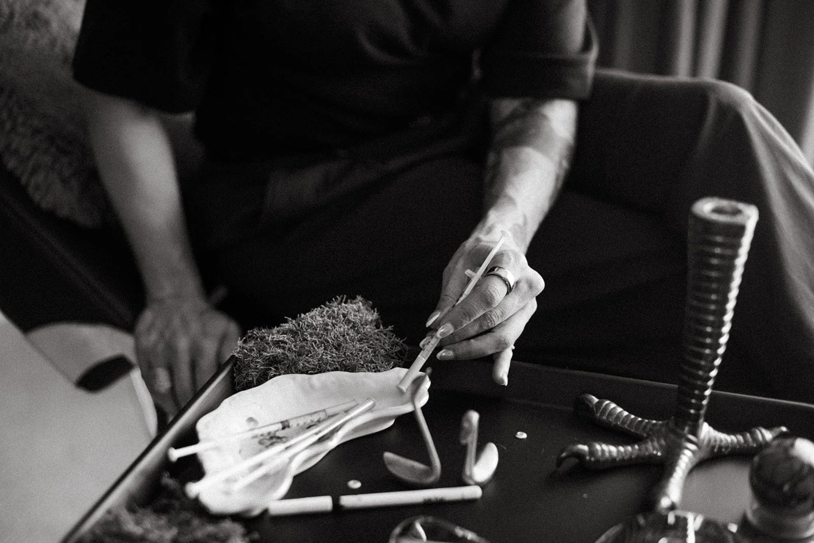 A person sitting on a chair, holding a tox injection needle above a scene like an altar. The scene is intentionally decorative for the photo.