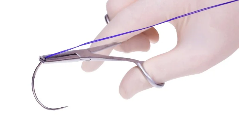 Close-up of a gloved hand holding a surgical needle with blue suture thread.