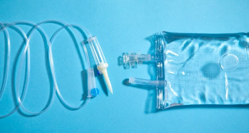 Medical IV tubing set and a sealed IV fluid bag on a blue background.