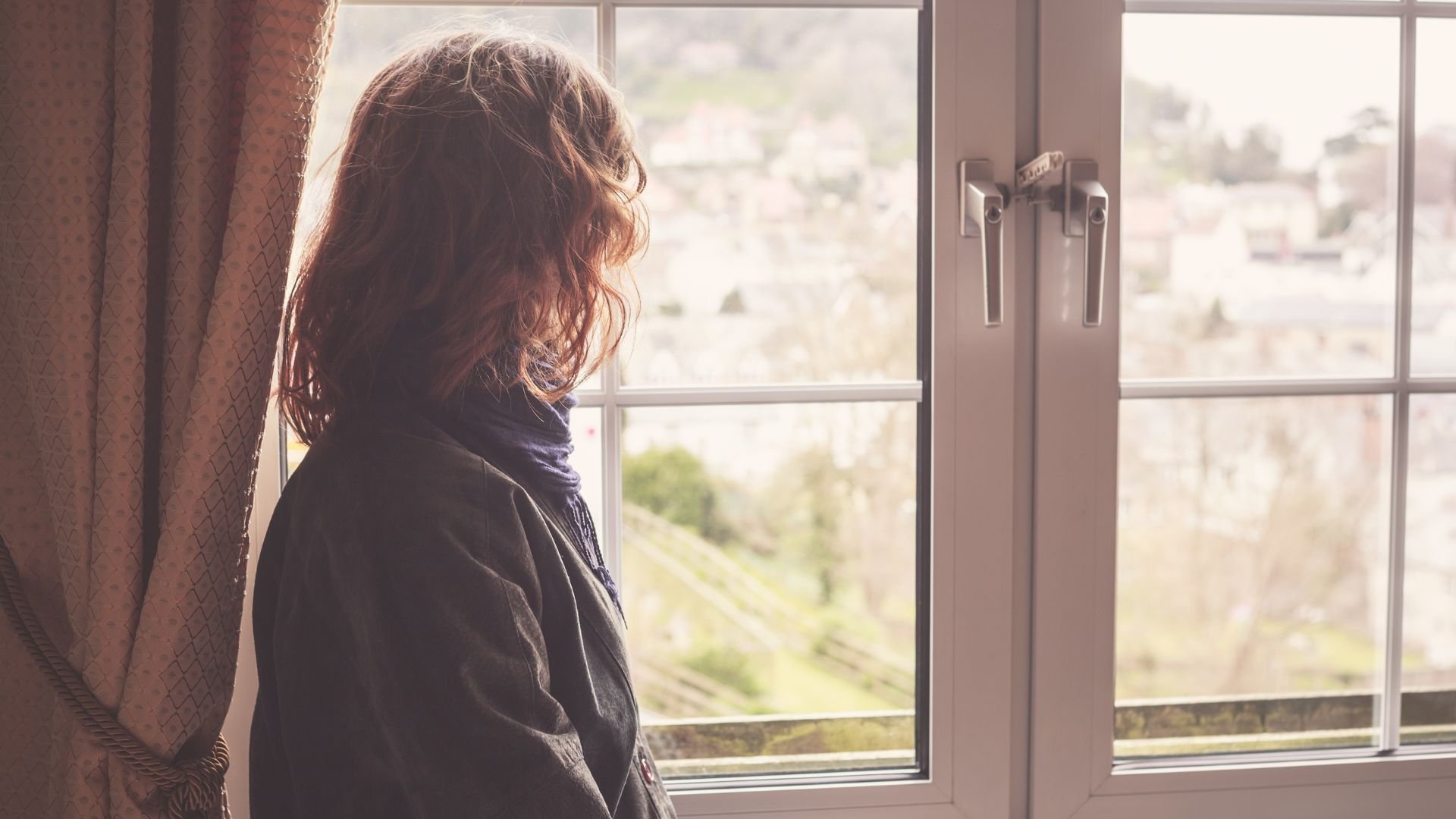 Person looking out a window in quiet reflection, representing self-understanding and personal growth in LGBTQIA+ affirming therapy.