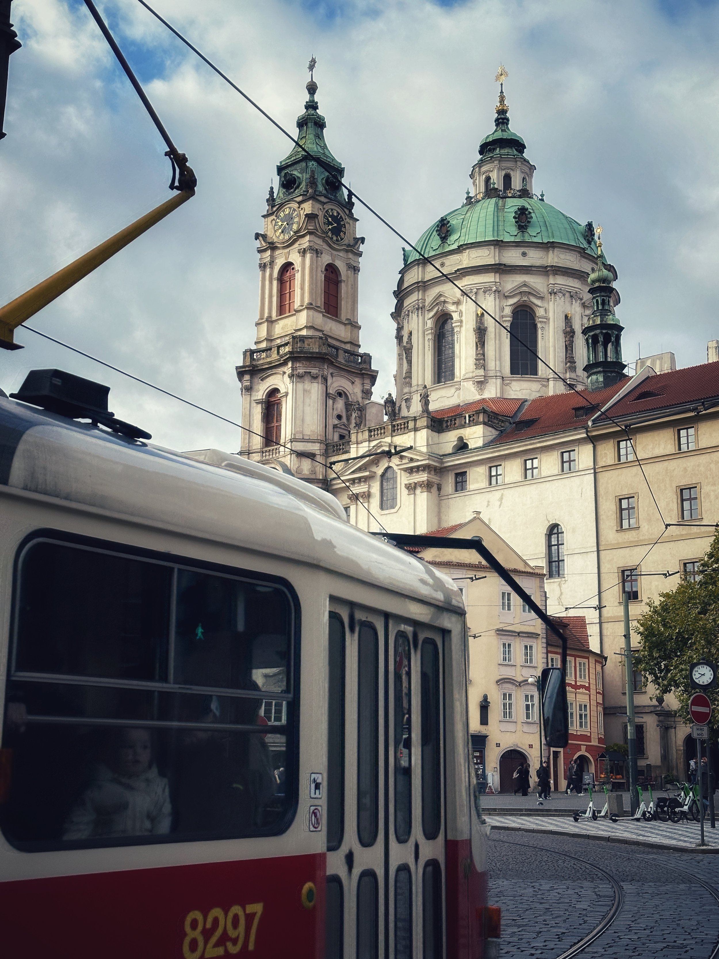 Tram passing through a street in Prague with a baroque church rising in the background.