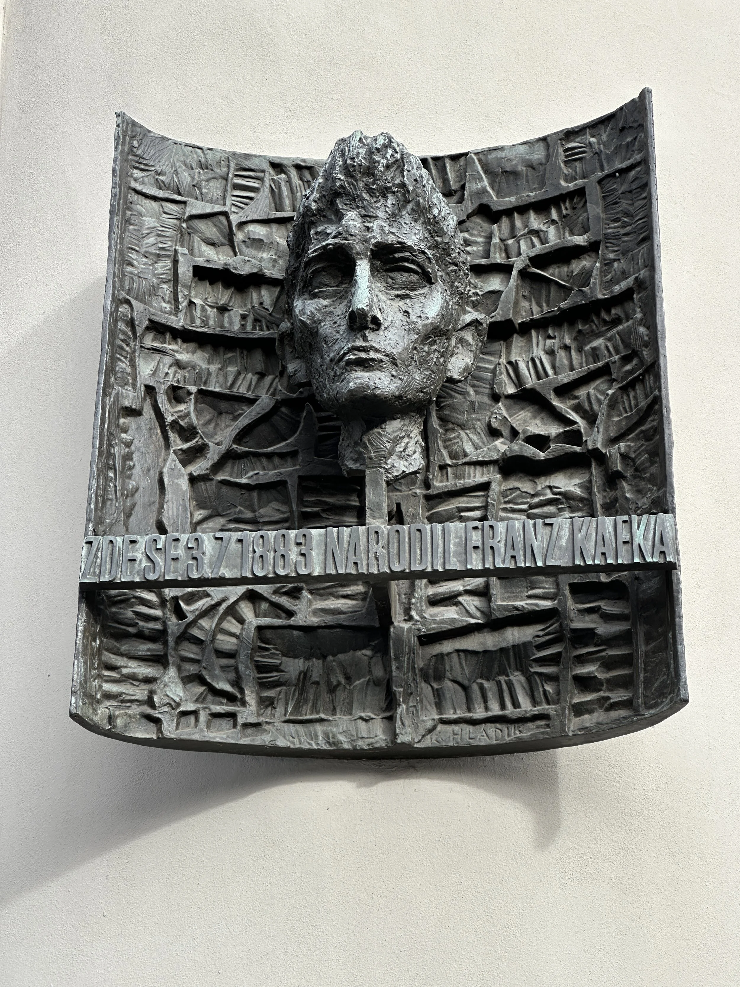 Bronze relief sculpture of Franz Kafka in Prague, photographed frontally against a pale wall.