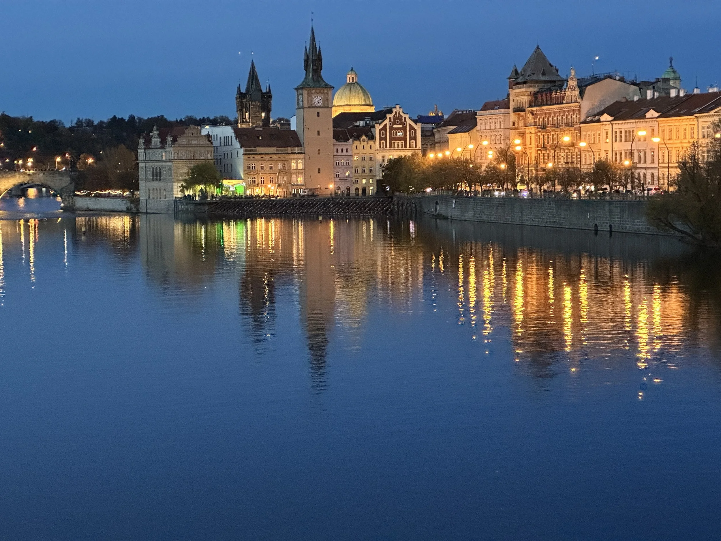 Prague skyline at dusk reflected on the Vltava River, city lights shimmering on the water