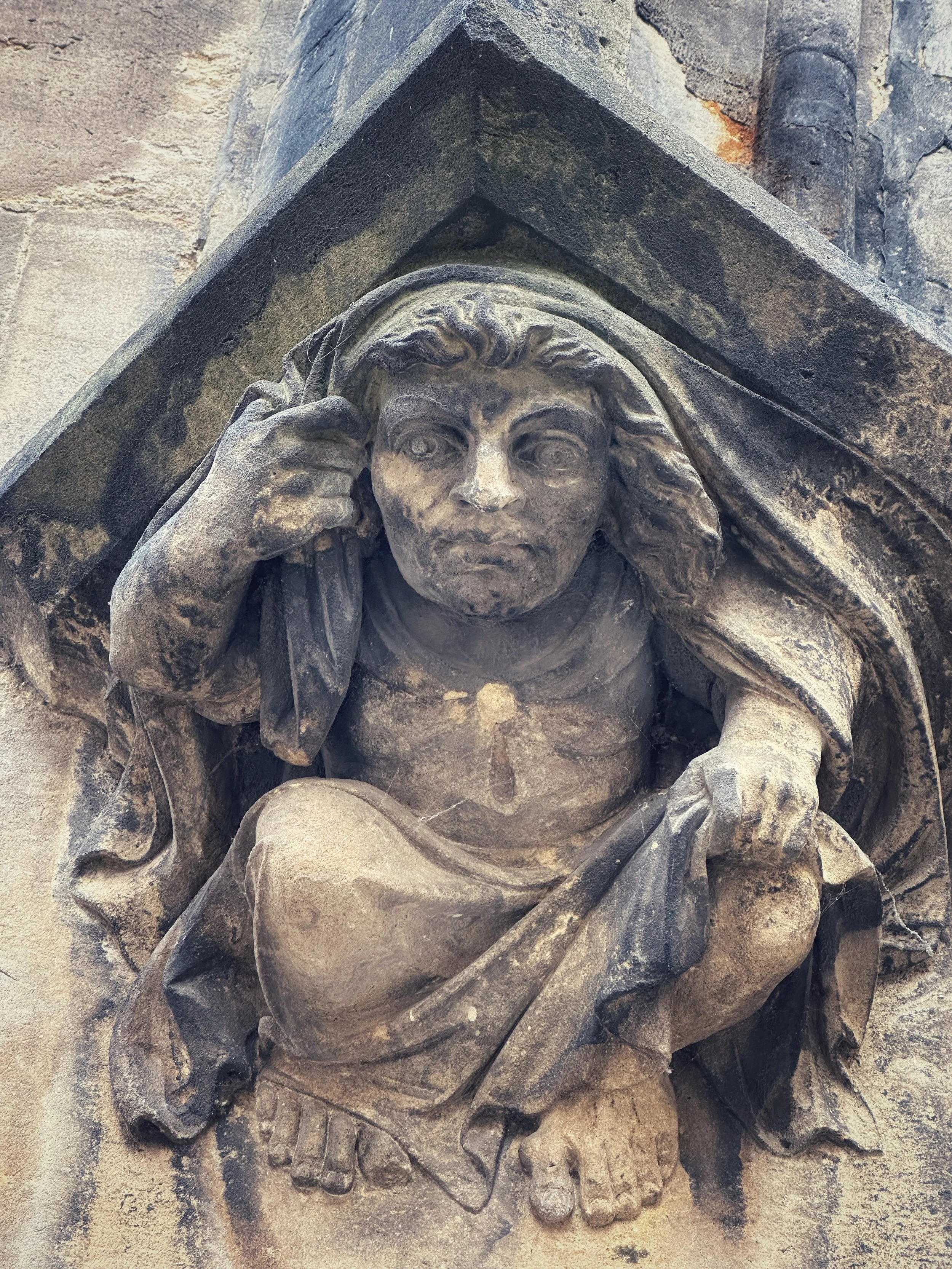 Stone sculpted figure embedded in a building façade in Prague, photographed in close detail.