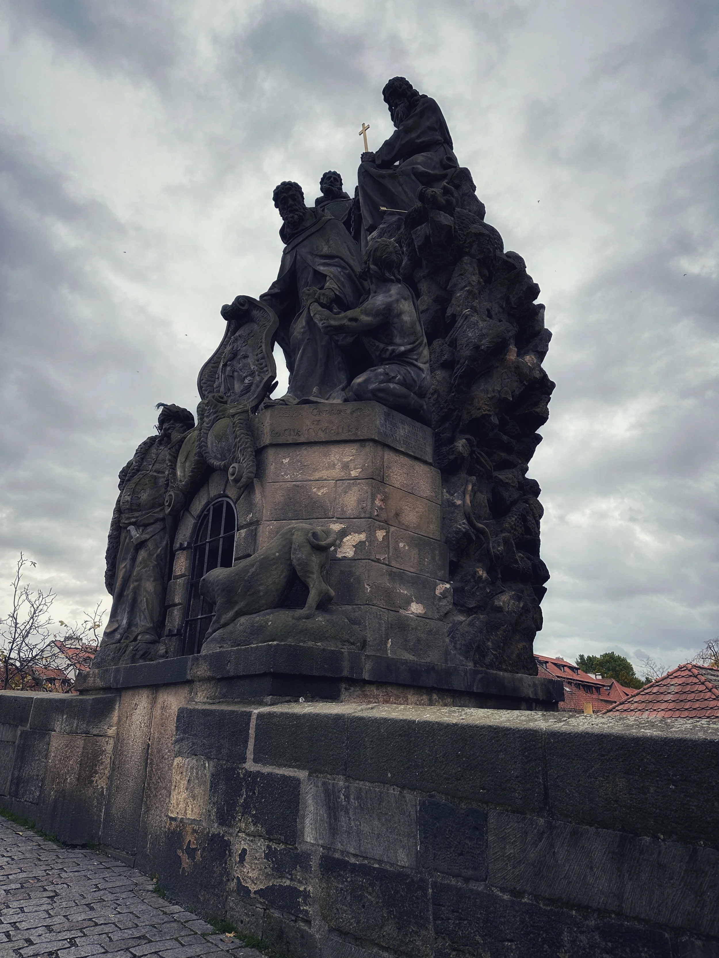 Baroque statue group on Charles Bridge in Prague under an overcast sky.