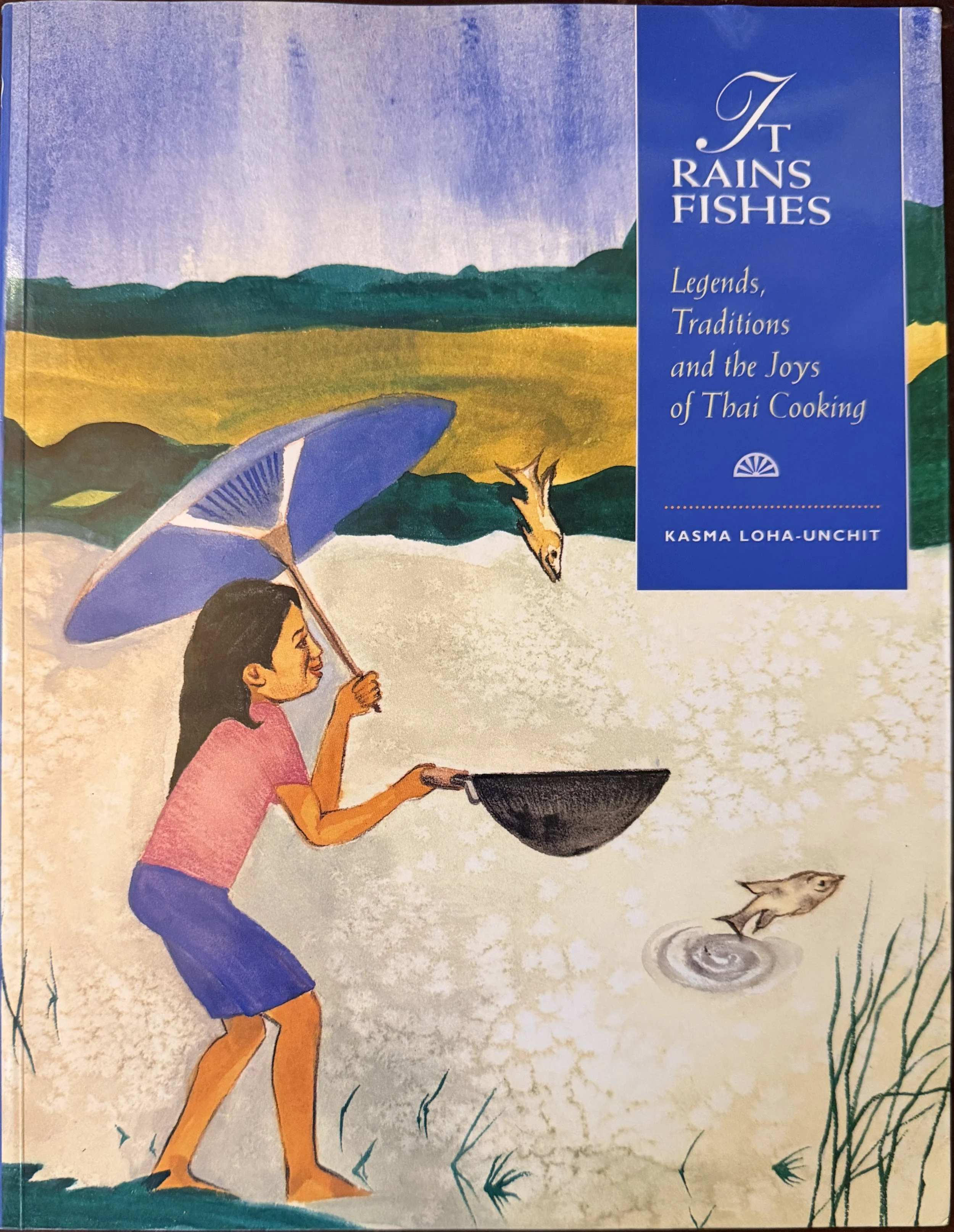 Cover of It Rains Fishes: Legends, Traditions and the Joys of Thai Cooking by Kasma Loha-Unchit, featuring an illustration of a girl catching fish falling from the sky with a wok.