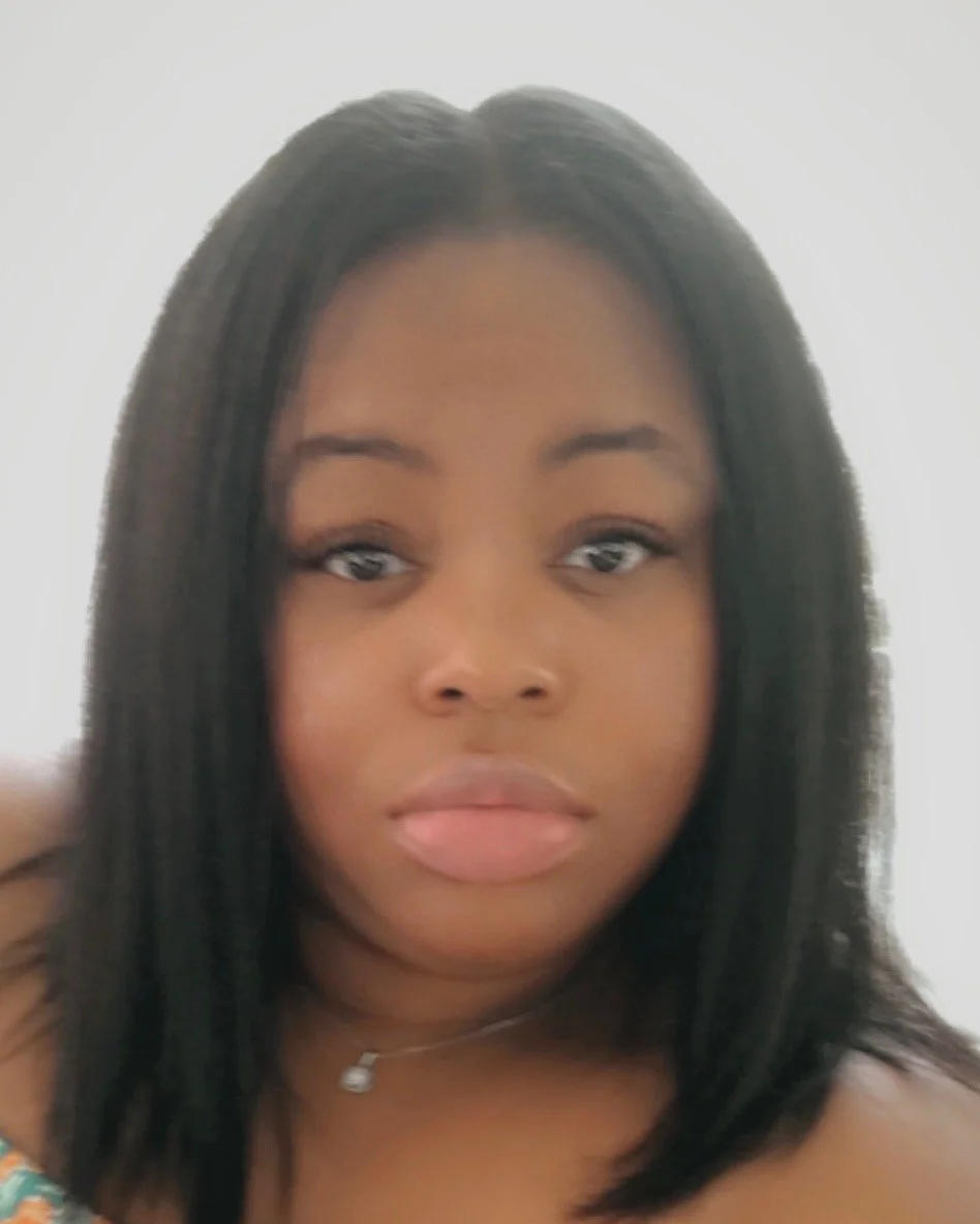 Close-up of a young woman with straight black hair, wearing a small necklace, slightly parted lips, and looking directly at the camera.