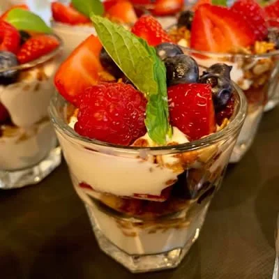 Dessert parfait with layered yogurt, mixed berries, granola, and a mint leaf in a glass