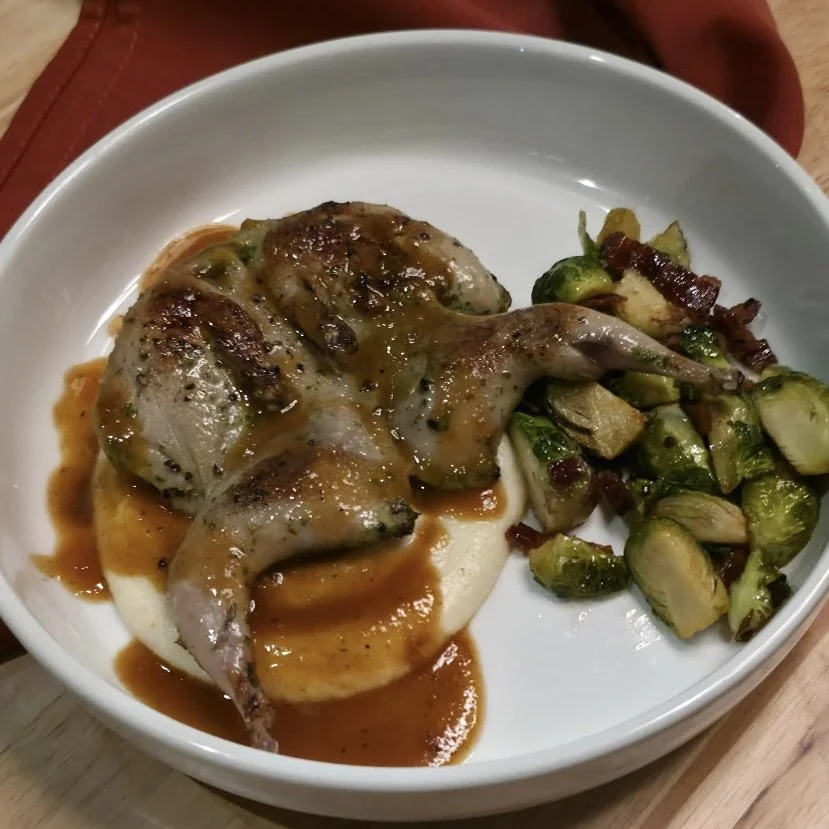 Cooked chicken leg with gravy, mashed potatoes, and roasted Brussels sprouts with bacon in a white bowl.