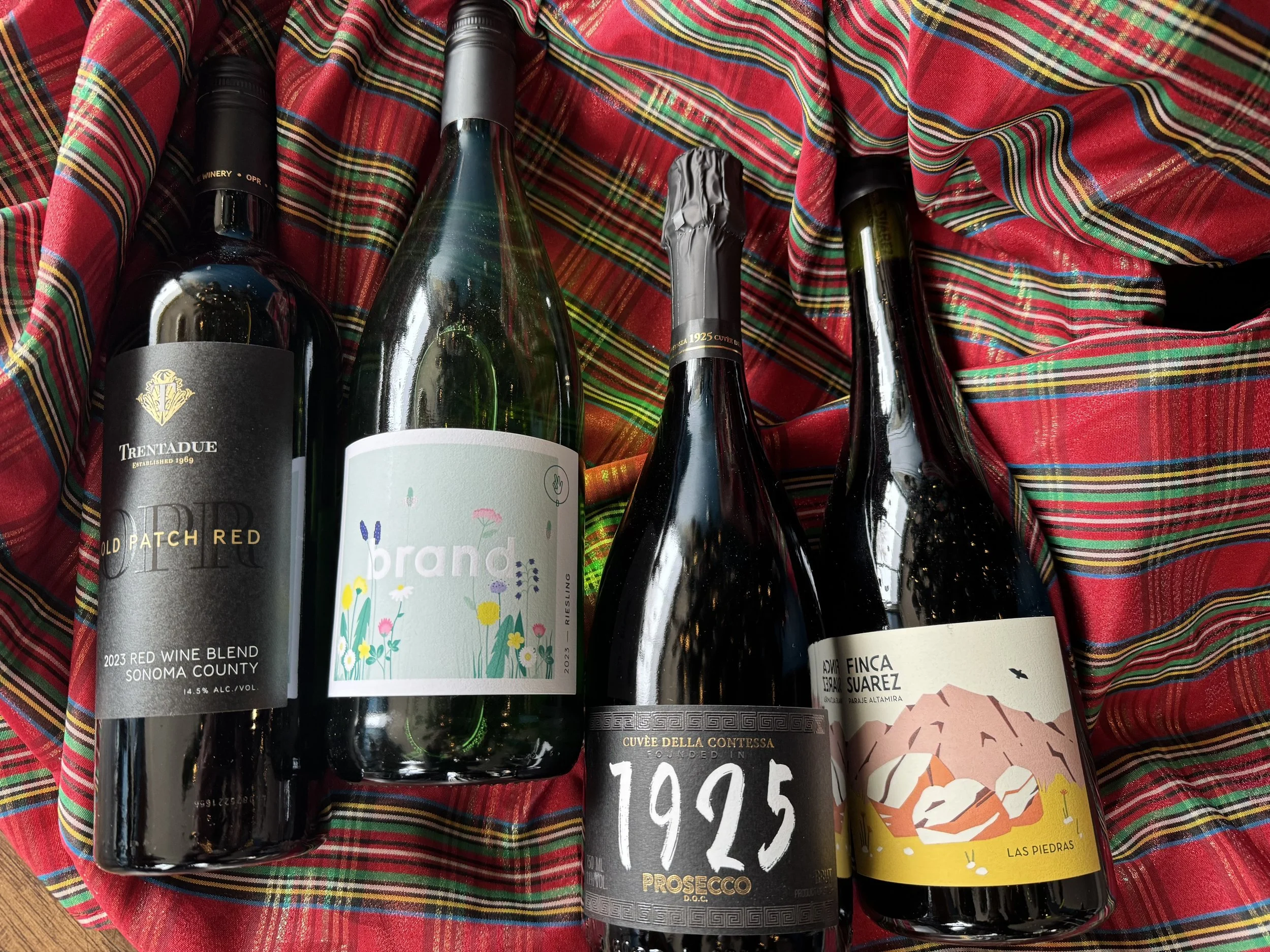 Five bottles of wine placed on a colorful, red plaid fabric.