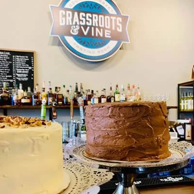 Decorative cakes displayed on a table at a venue with a 'Grassroots & Vine' sign and bar shelves in the background.
