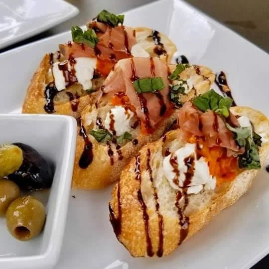 Three crostini topped with smoked salmon, whipped cheese, chopped herbs, and balsamic glaze.