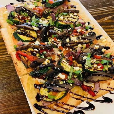 Flatbread topped with roasted zucchini, red peppers, onions, chopped herbs, crumbled cheese, and drizzled with balsamic glaze.