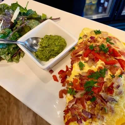 Omelette topped with tomatoes, onions, and herbs, served with a side of mixed greens and green sauce