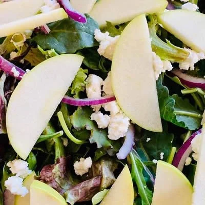 Mixed green salad with apple slices, crumbled cheese, and purple onion slices.