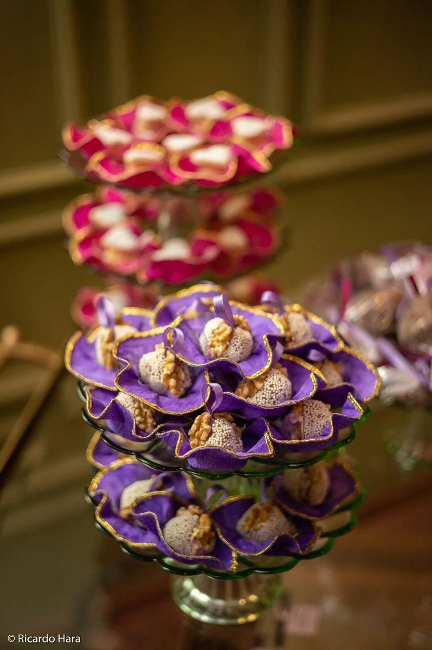 Taças decoradas com doces enfeitados e acabamento dourado, em cores roxa e rosa, exibindo doces e biscoitos em louças de suporte decorativos.