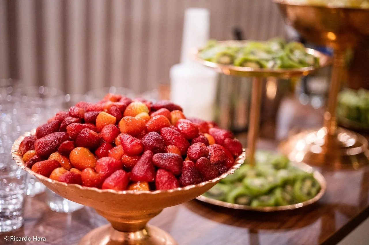 Frutas vermelhas em uma tigela de mesa, com outros pratos de frutas ao fundo.