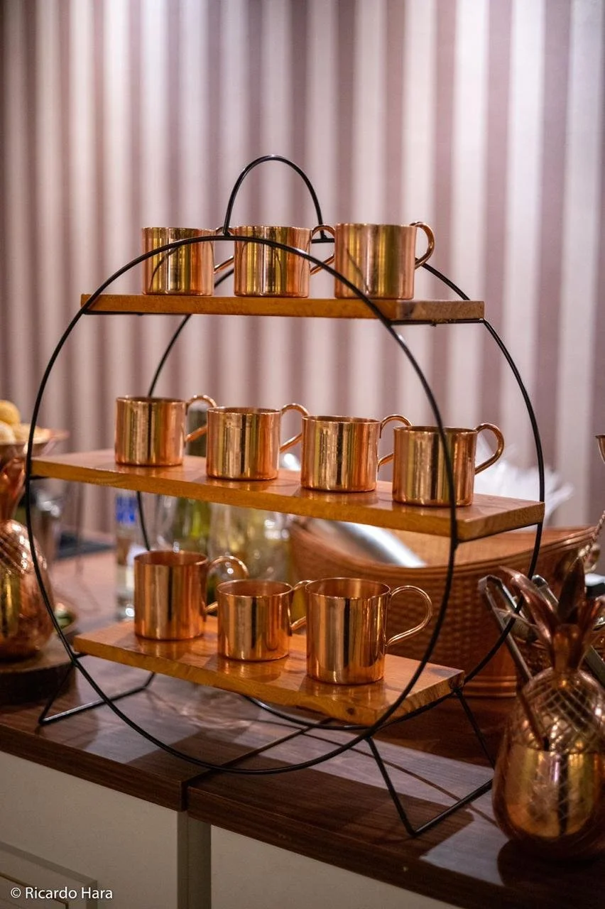 Conjunto de canecas de metal com acabamento dourado, organizadas em uma estrutura de suporte com três prateleiras de madeira.