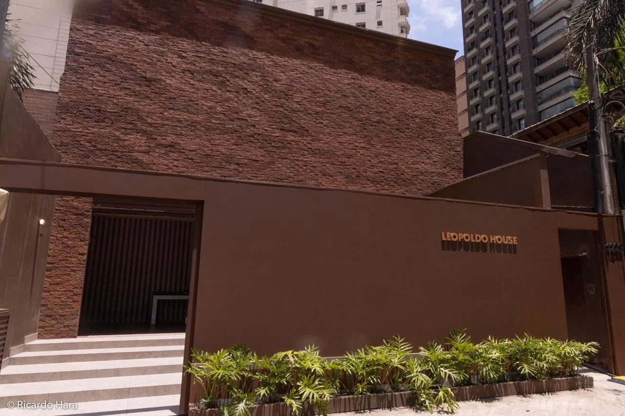 Fachada moderna do edifício Leopoldo House com nome na parede e plantas na frente.