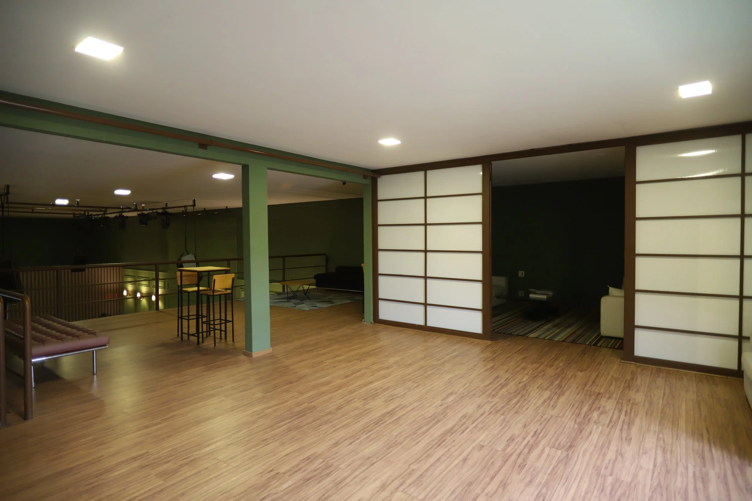 Sala com piso de madeira, divisórias de portas de papel estilo shoji, canto de sofá branco, mesa de centro e área com televisão ao fundo. Mezanino Lounge com sala privativa: Sala da noiva, Sala de debutante ou sala vip de palestrante.