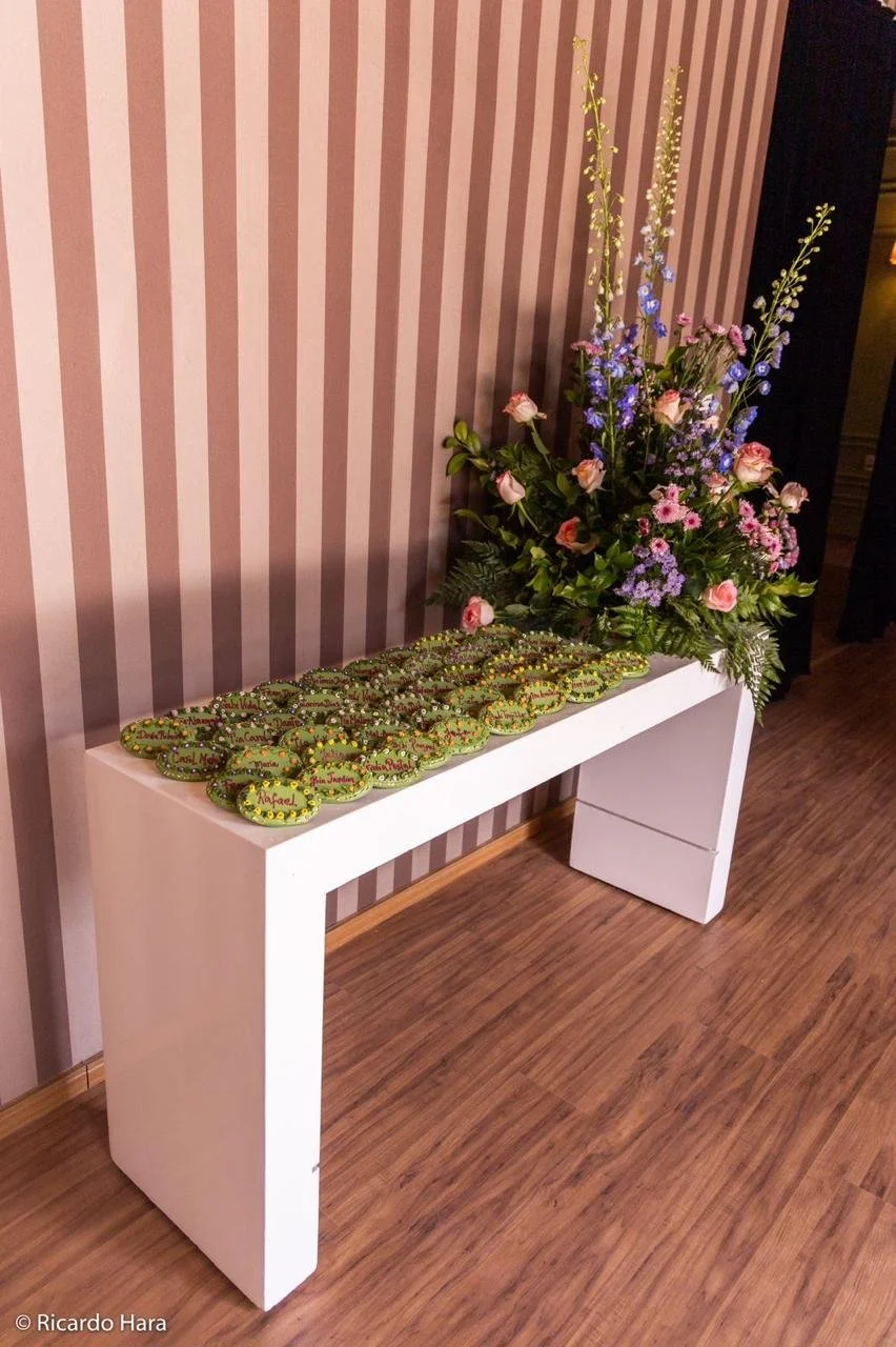 Mesa branca com pedras decorativas e um arranjo de flores em fundo de parede com listras rosa e bege.
