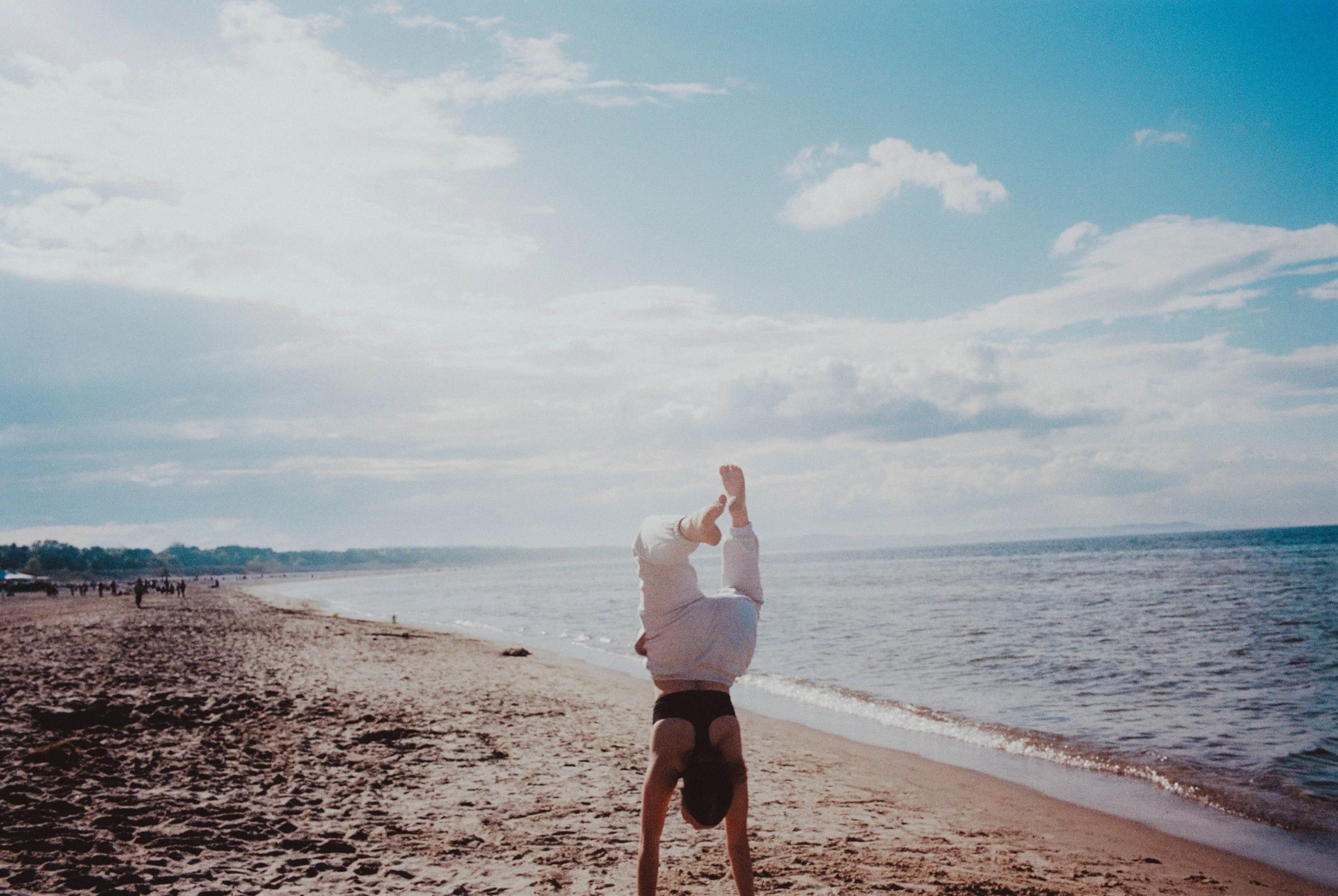 Jemand macht einen Handstand am Strand bei Sonnenaufgang oder Sonnenuntergang, mit Blick aufs Meer und bewölktem Himmel.