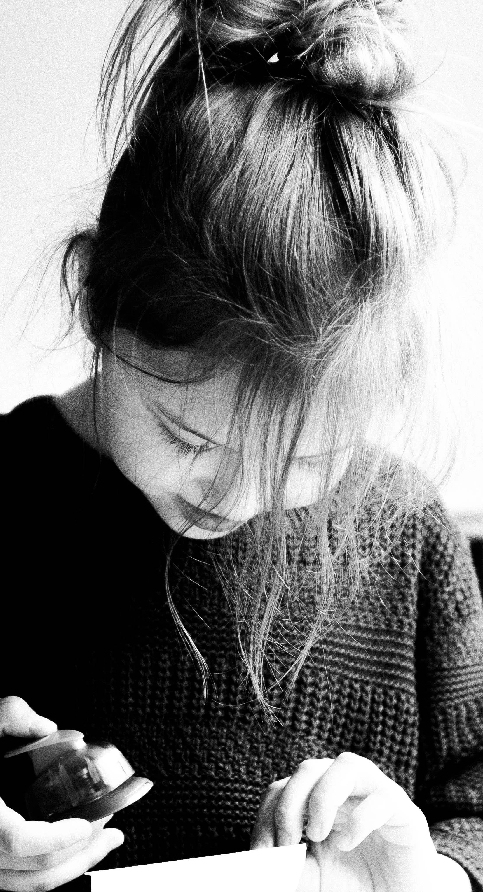 Schwarz-weiß-Foto eines Mädchens mit zerzaustem Haar, das auf eine Tasse schaut, die sie in der Hand hält.