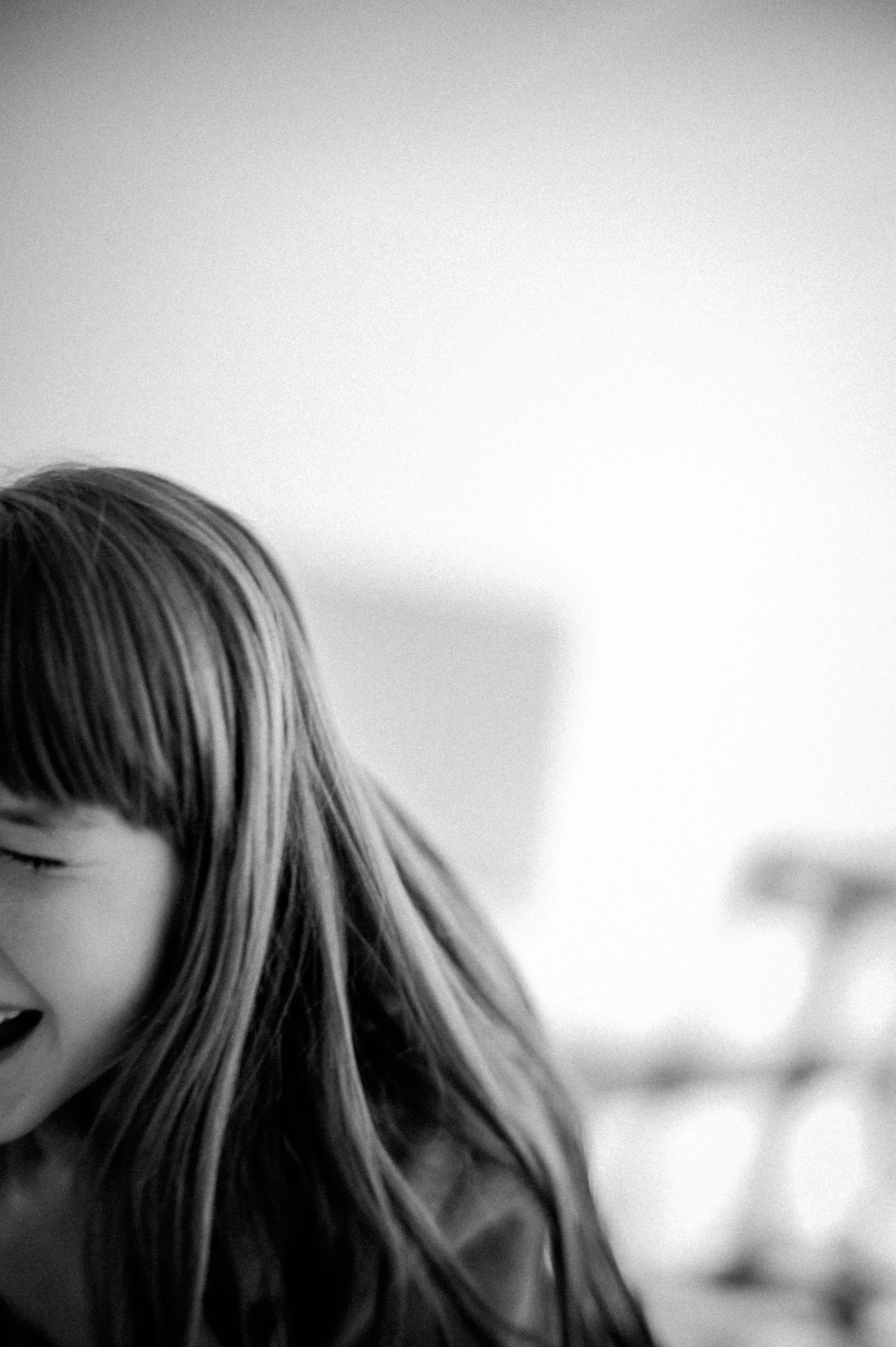 Ein lachendes junges Mädchen mit langen Haaren in einem schwarzen und weißen Foto, halb von der Seite sichtbar, mit einem freundlichen Gesichtsausdruck.