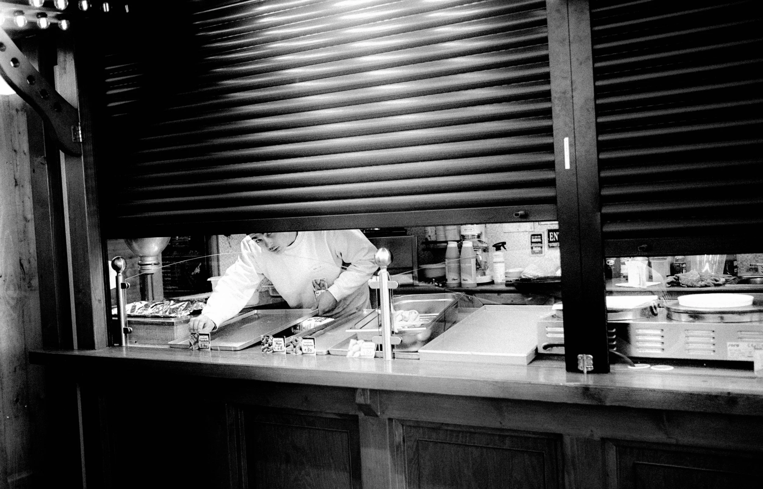 Ein Koch in einer Küche, sichtbar durch ein halb geöffnetes Rolltor, beim Vorbereiten von Lebensmitteln.