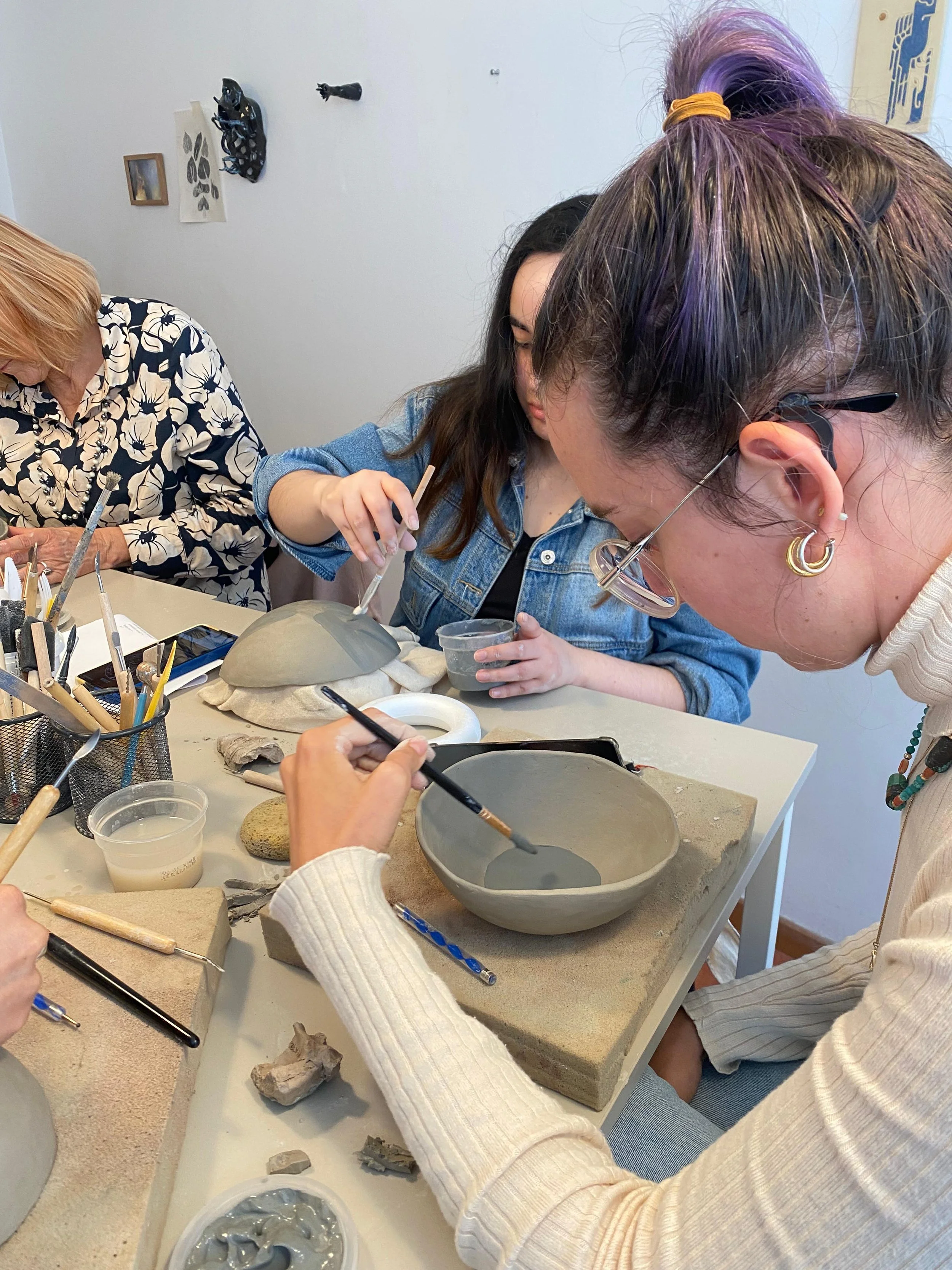 Grupo de personas trabajando en una clase de cerámica, aplicando arcilla sobre moldes y utensilios de cerámica en una mesa.