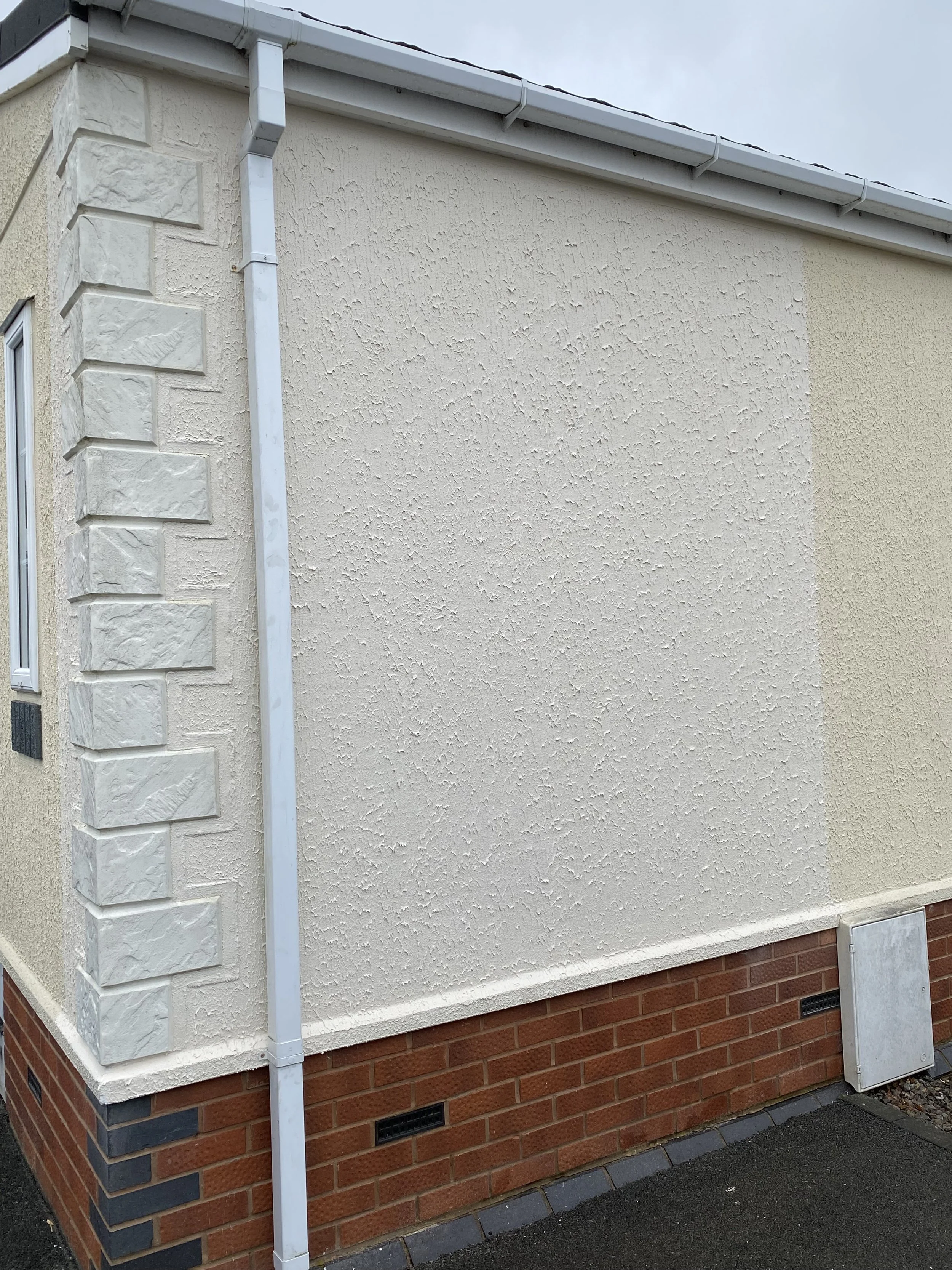 Corner of a building with textured cream-colored walls, brick foundation, and metal gutter system.