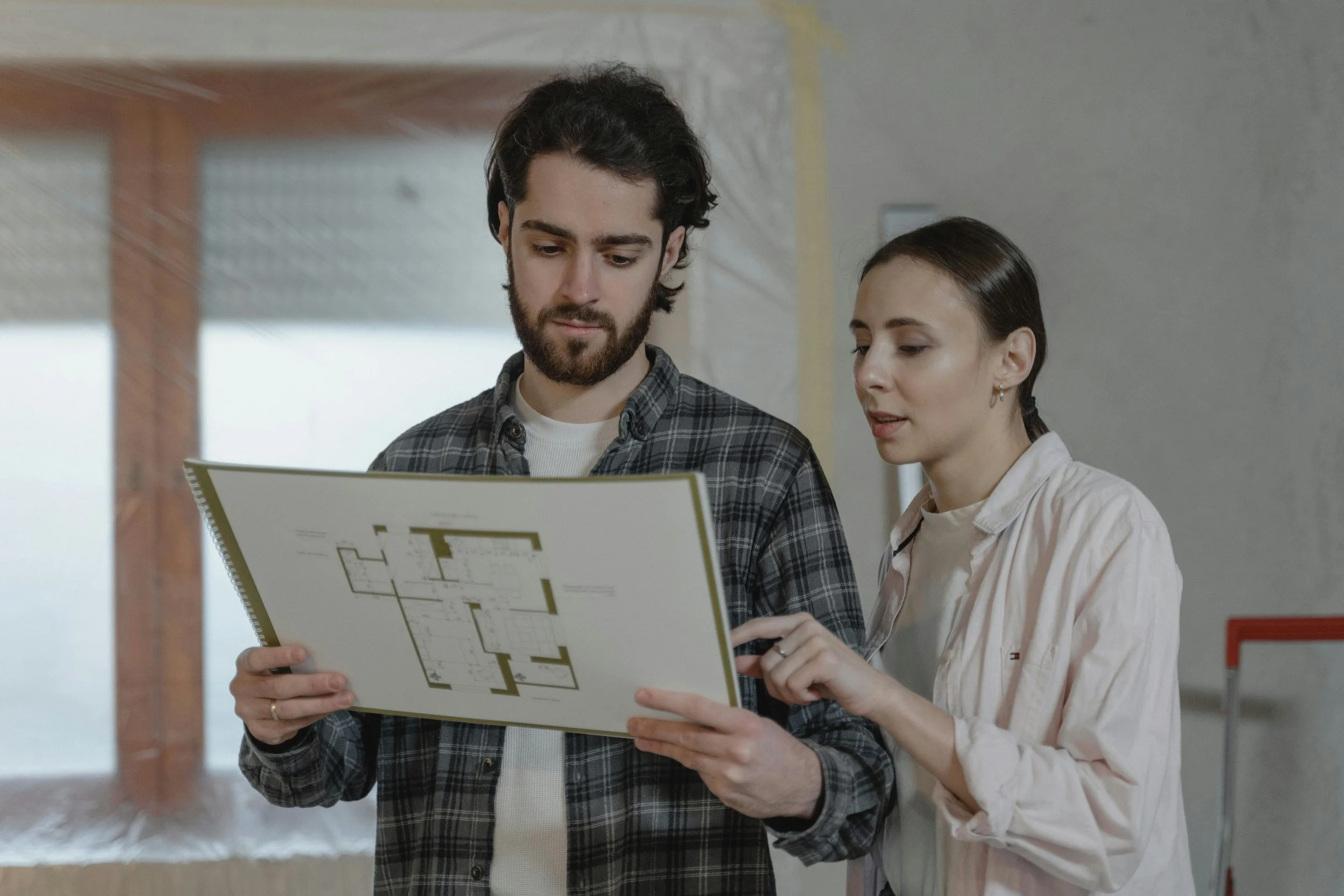 Two people review a building floor plan together, carefully discussing layout details. Reflecting the perspective of Steven Jermoluk on accurate estimating.