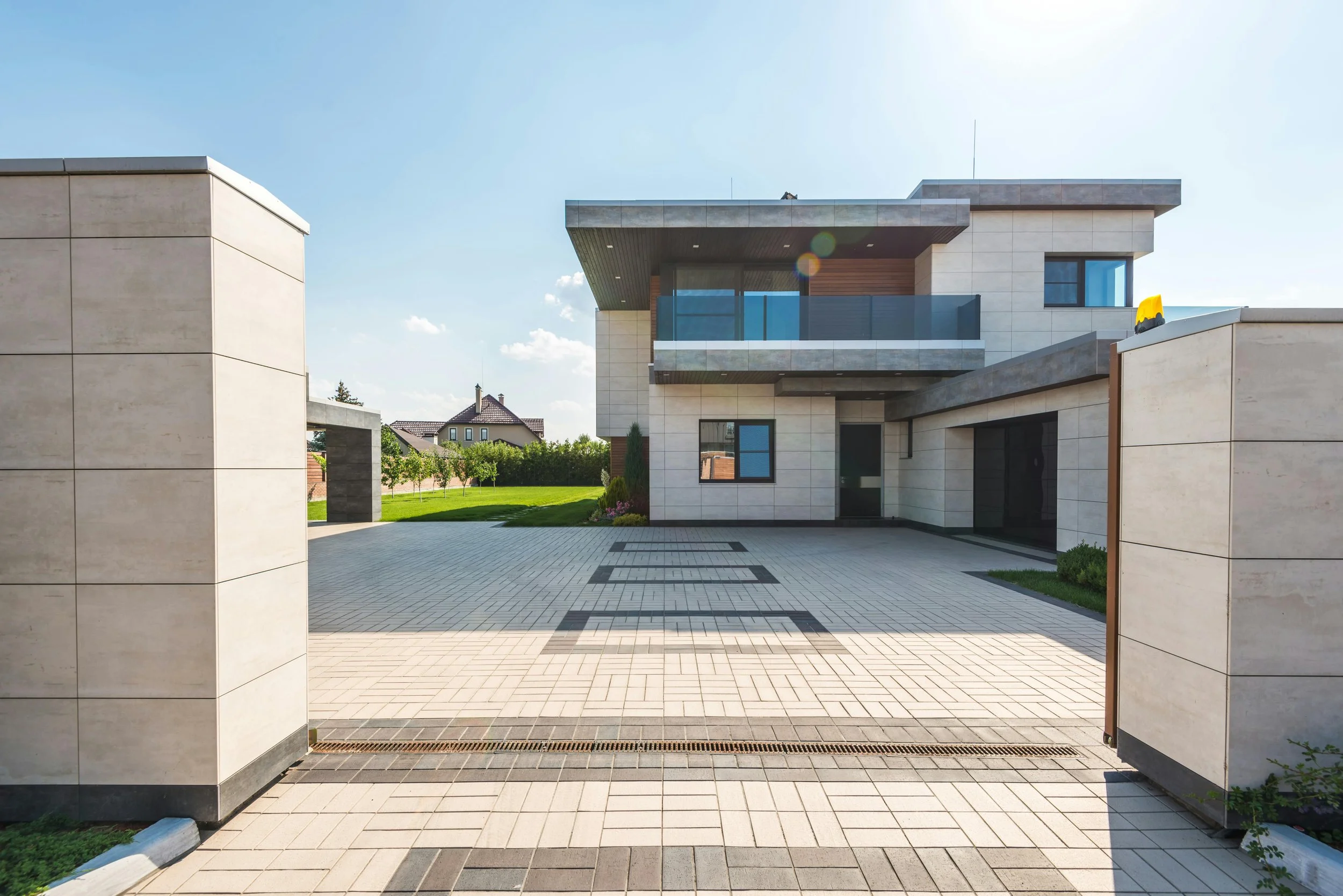 A modern two-story house with clean lines and large glass windows is seen behind an open gate. Reflecting the perspective of Steven Jermoluk on navigating hidden costs in residential budgets.