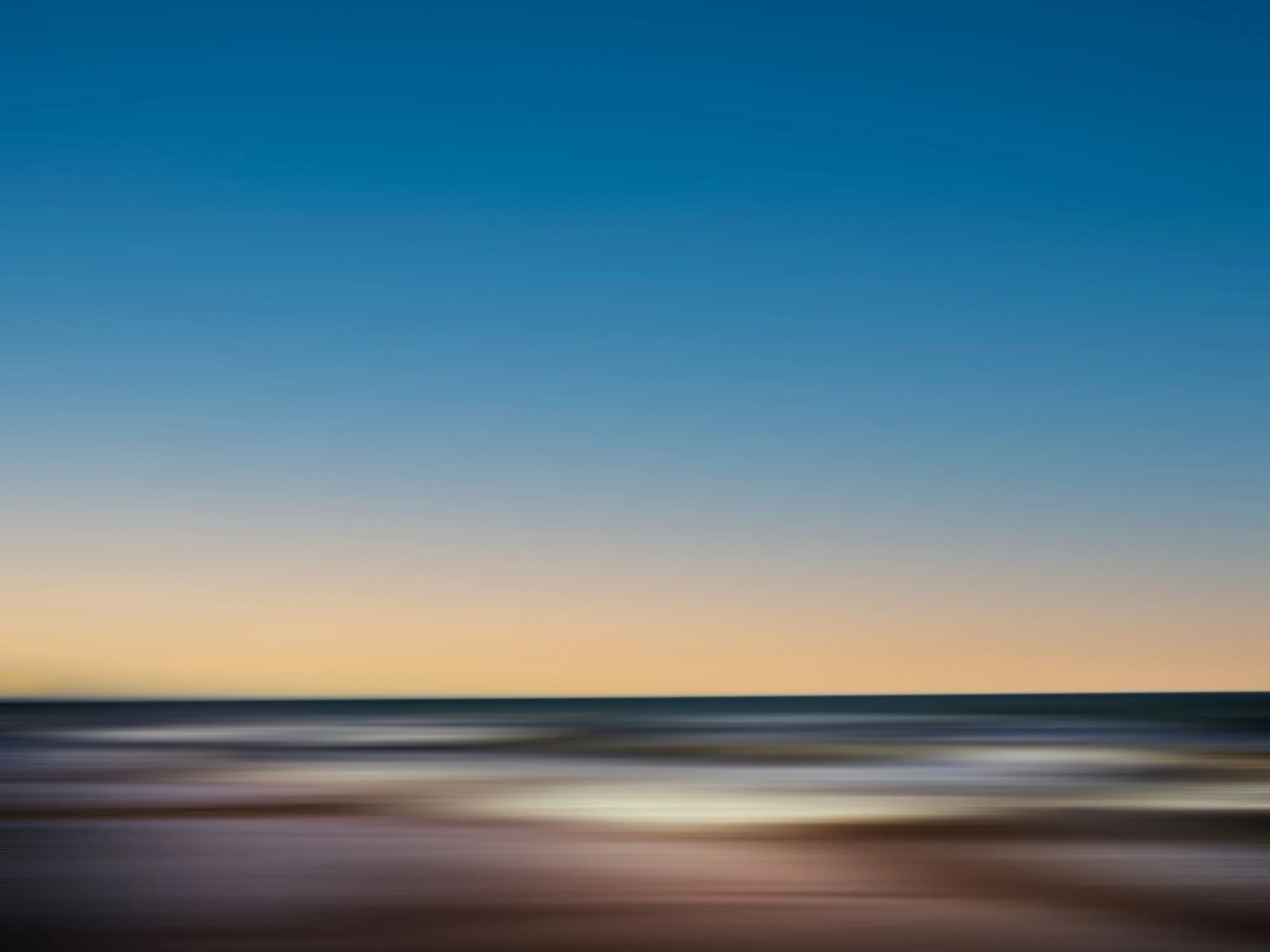 Imagen borrosa de un paisaje con cielo azul y un horizonte difuso, con tonos cálidos en la parte inferior.
