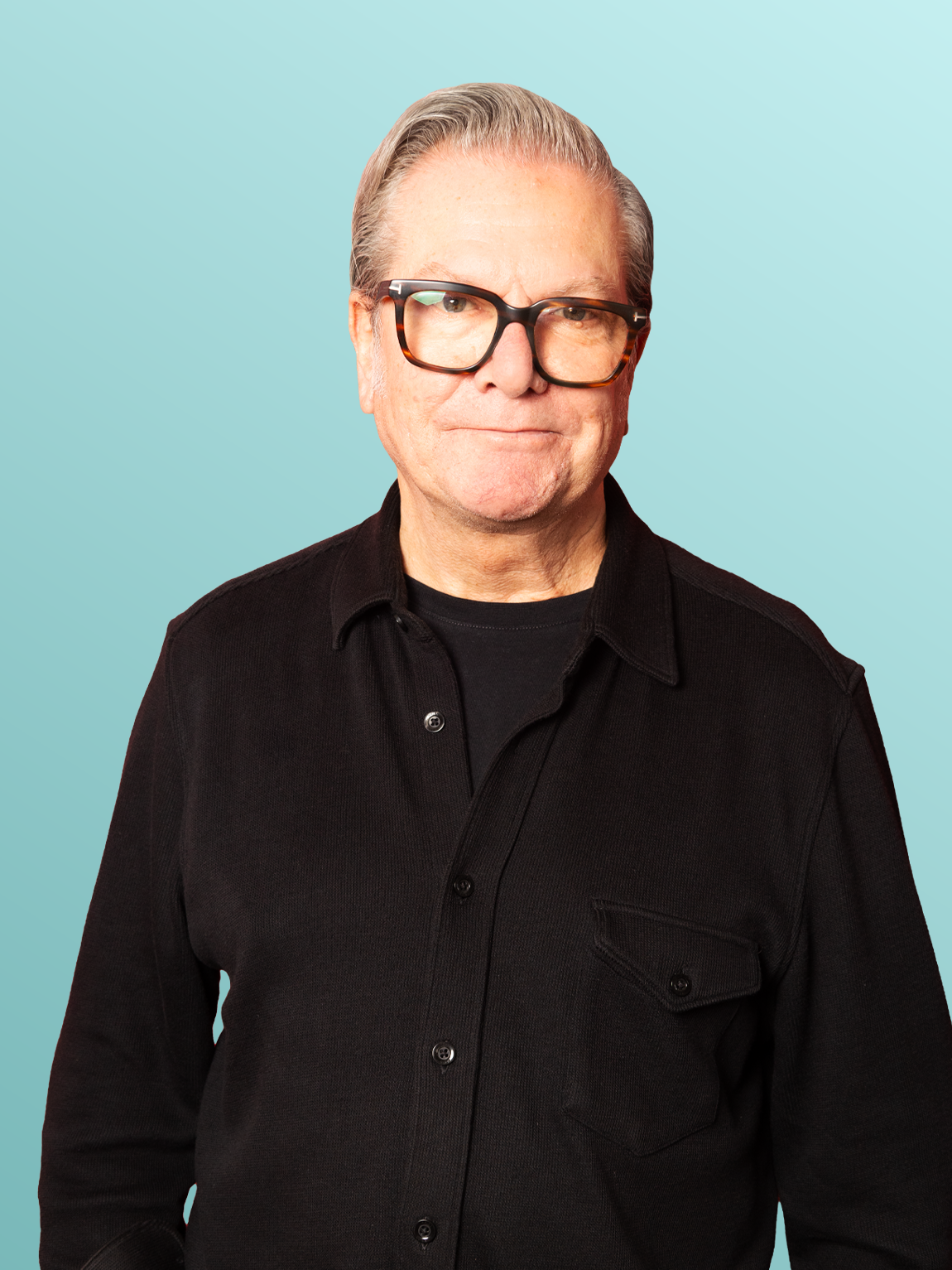 A middle-aged man with gray hair, wearing glasses and a black shirt, posing against a light blue background.