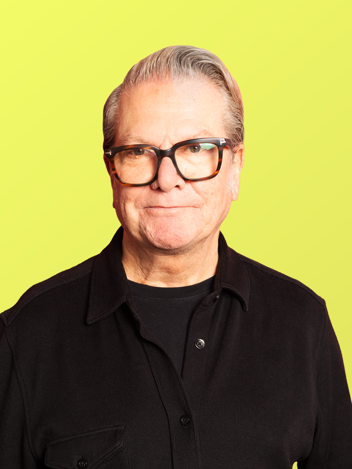 A middle-aged man with gray hair, wearing glasses and a black shirt, posing against a light blue background.