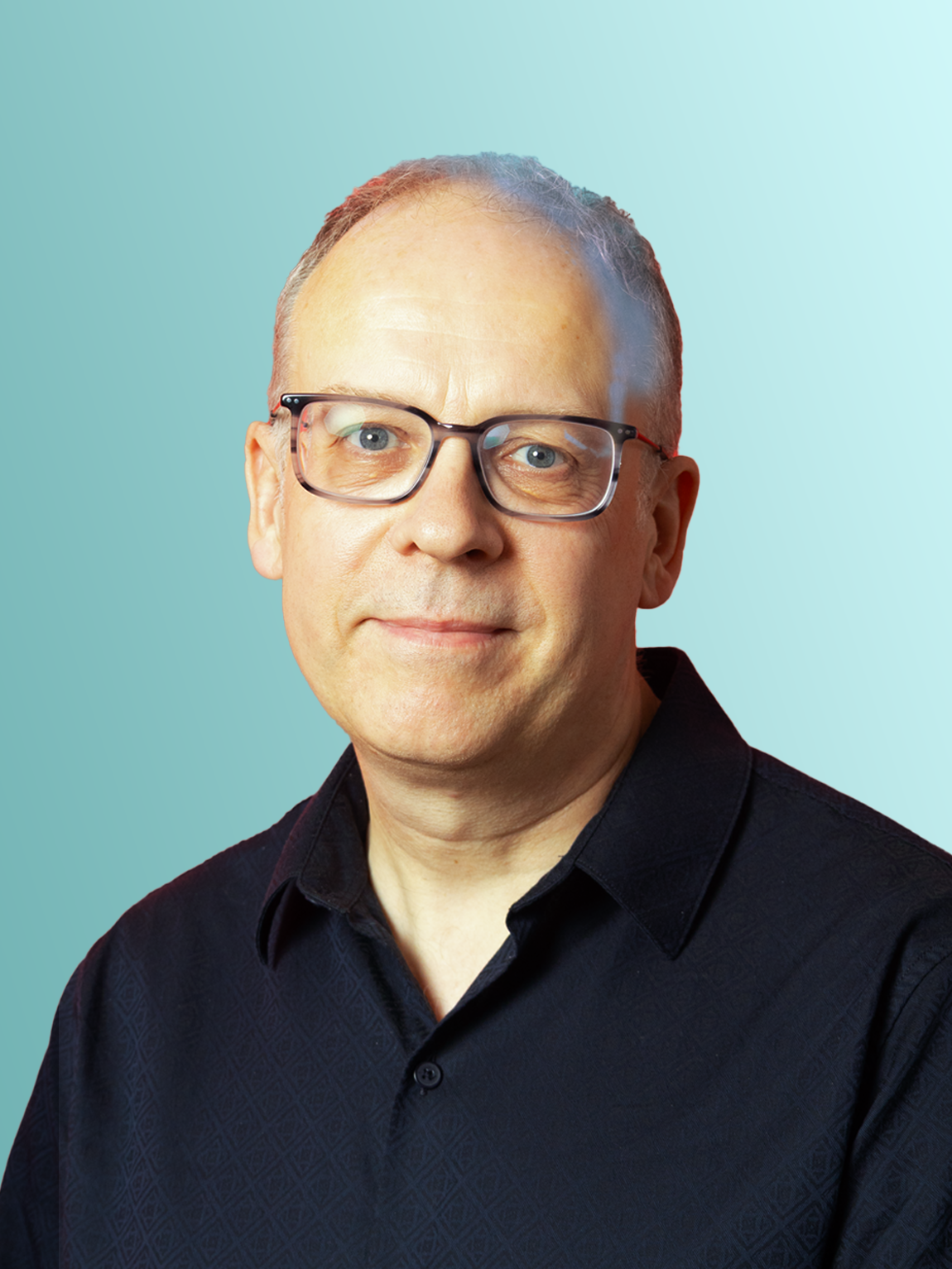 A man wearing glasses and a black button-up shirt stands against a light blue background.