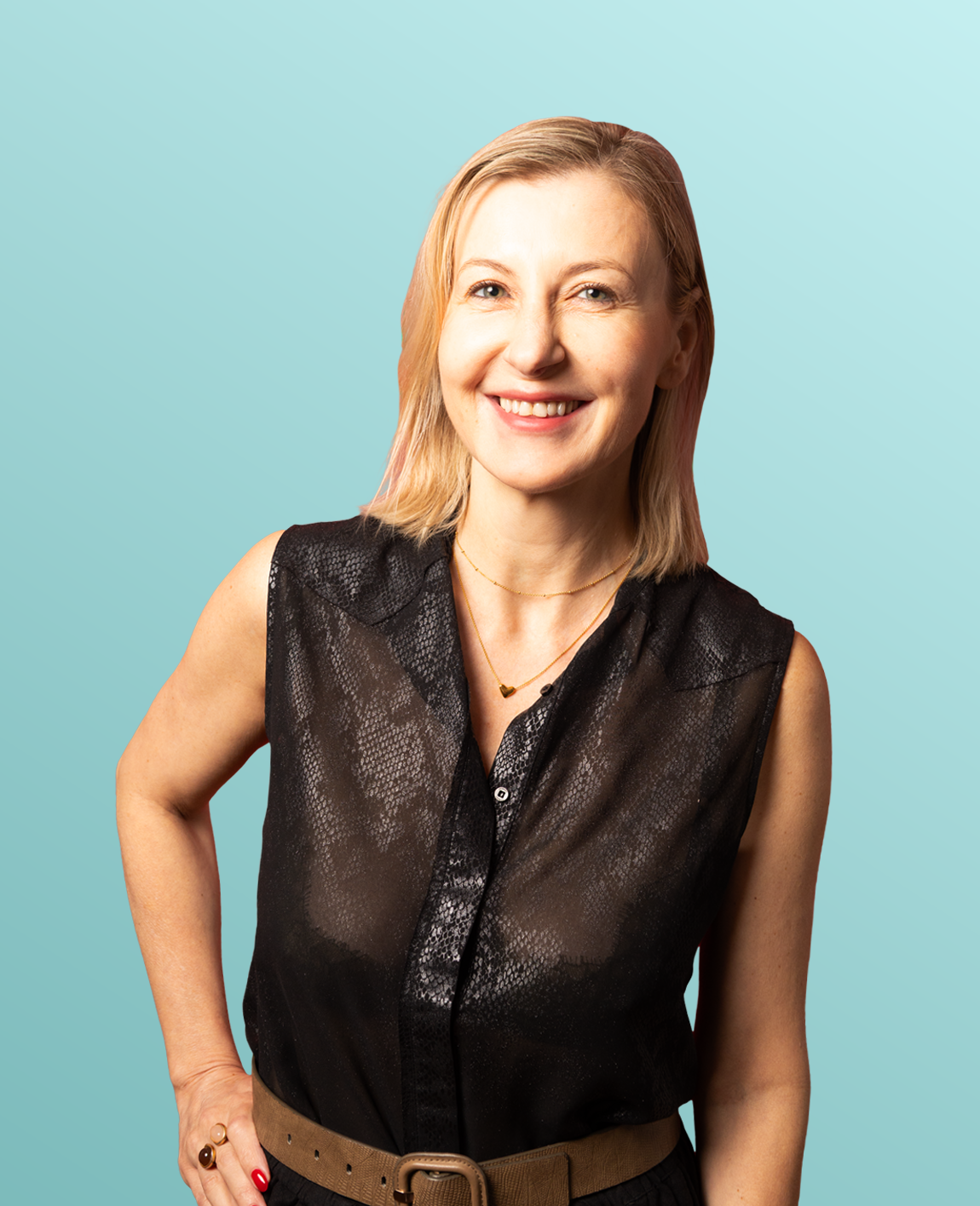 A woman with blonde hair, wearing a sleeveless black top with a textured pattern, a brown belt, and jewelry, smiling against a yellow background.