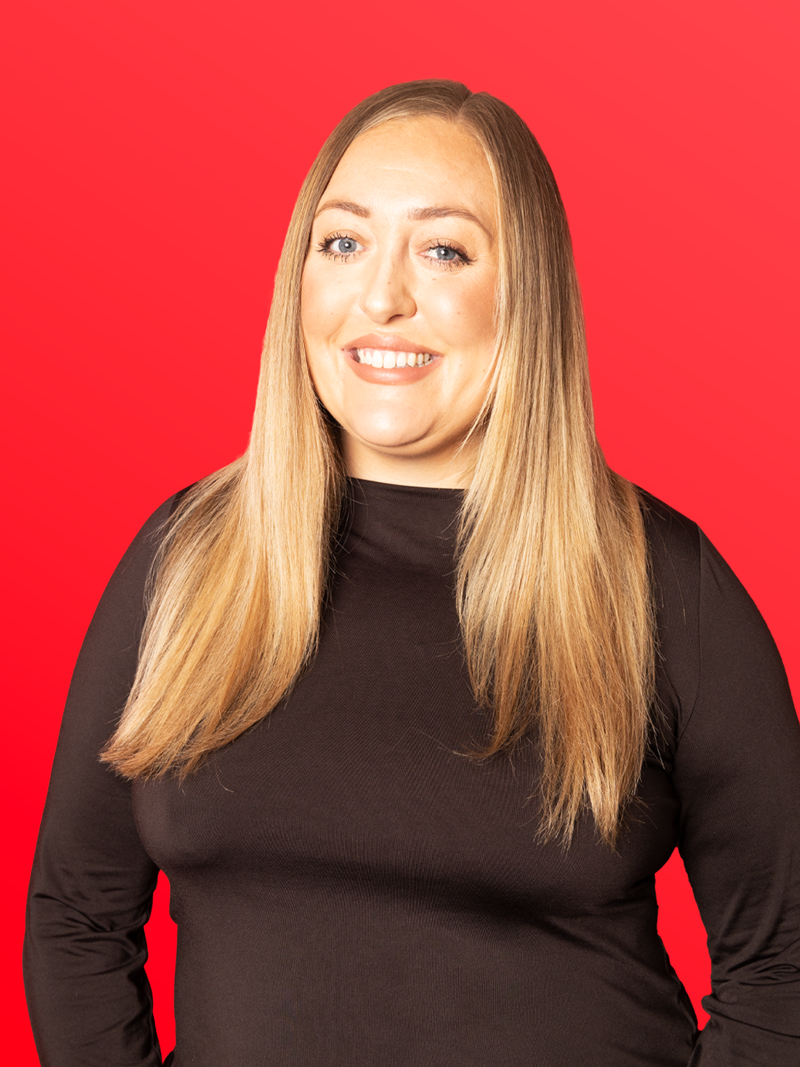 A woman with long blonde hair wearing a black top, smiling against a red background.