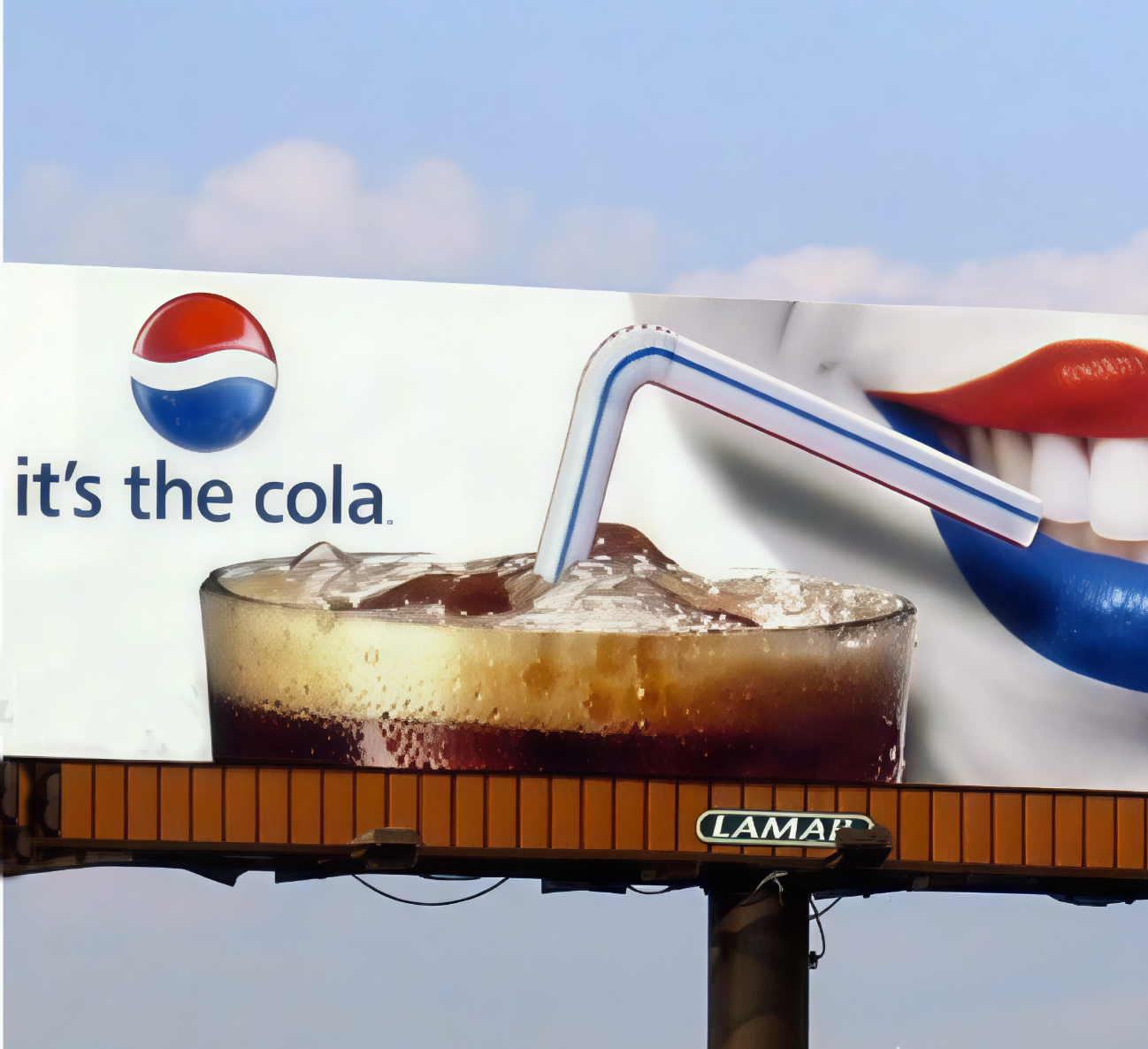 Billboard advertisement featuring a glass of cola with ice and a straw, and lips painted in red and blue drinking through the straw. Text reads 'it's the cola.' with a Pepsi logo.