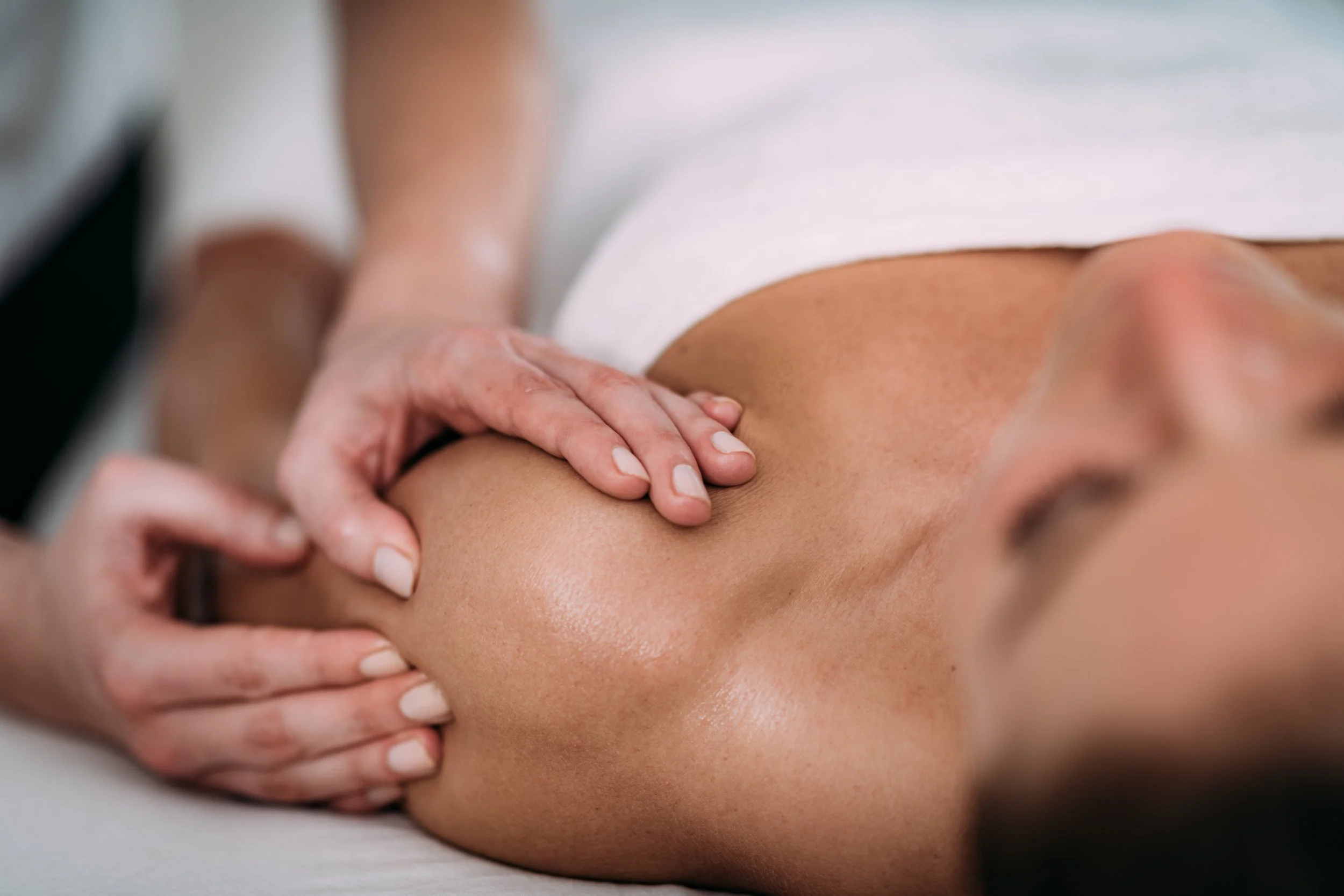 A woman receives a back massage from a massage therapist in a spa setting, lying face down on a massage table with a white towel. Beneficial for riders to receive therapeutic massage for increased performance.