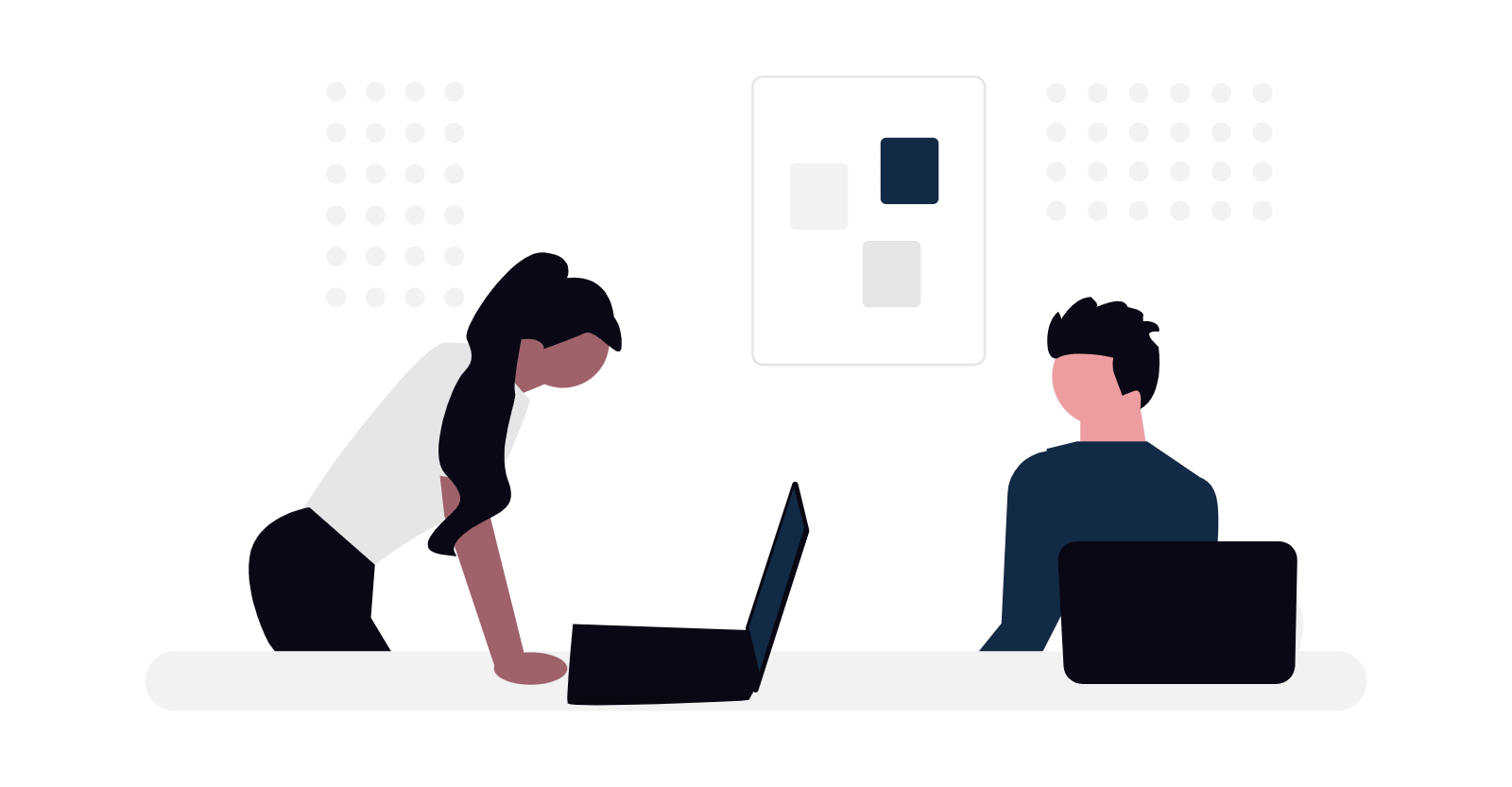 Woman leaning over a desk with two laptops, discussing with a seated man.