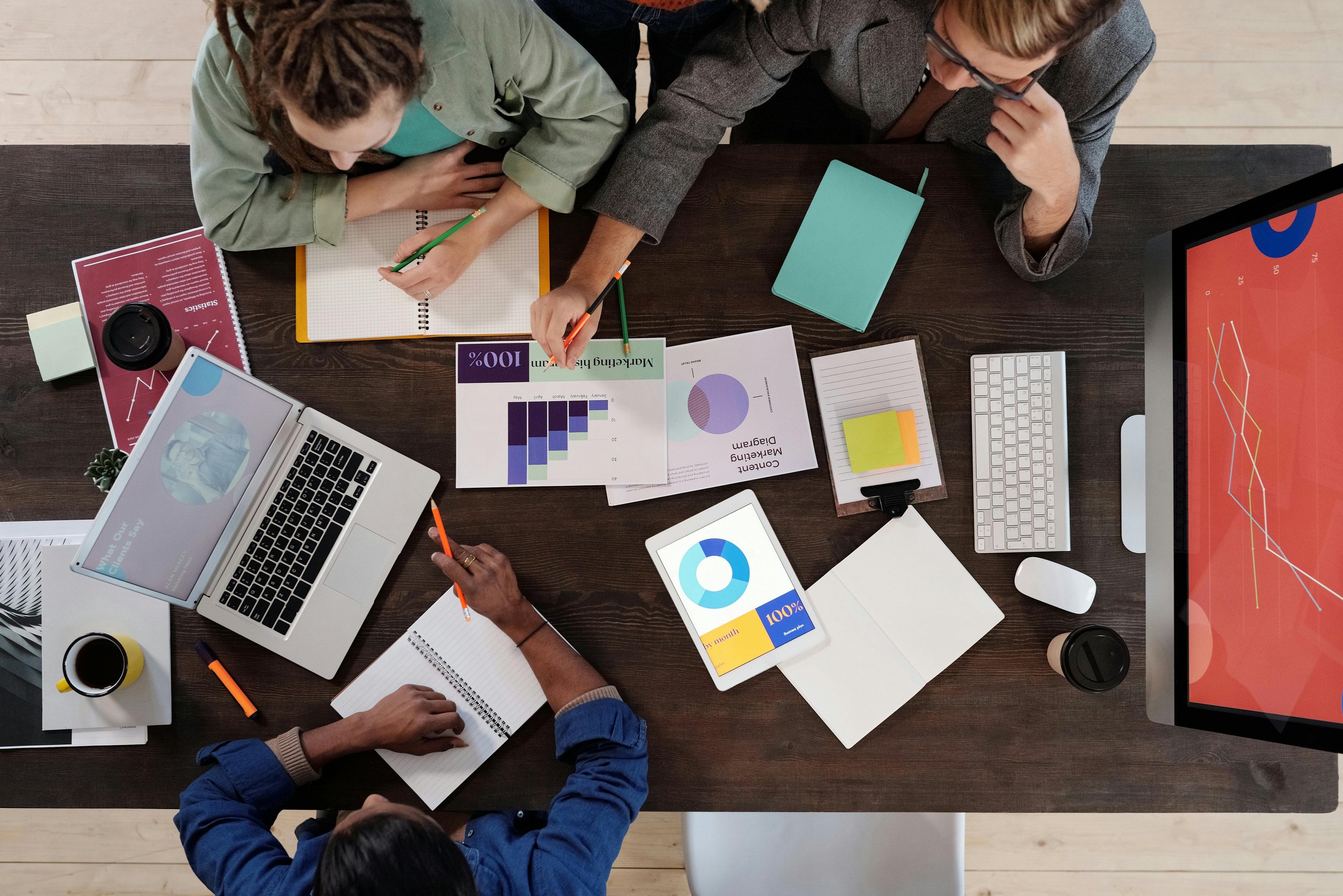 Group of people collaborating at a desk with charts, notebooks, laptops, and marketing materials.