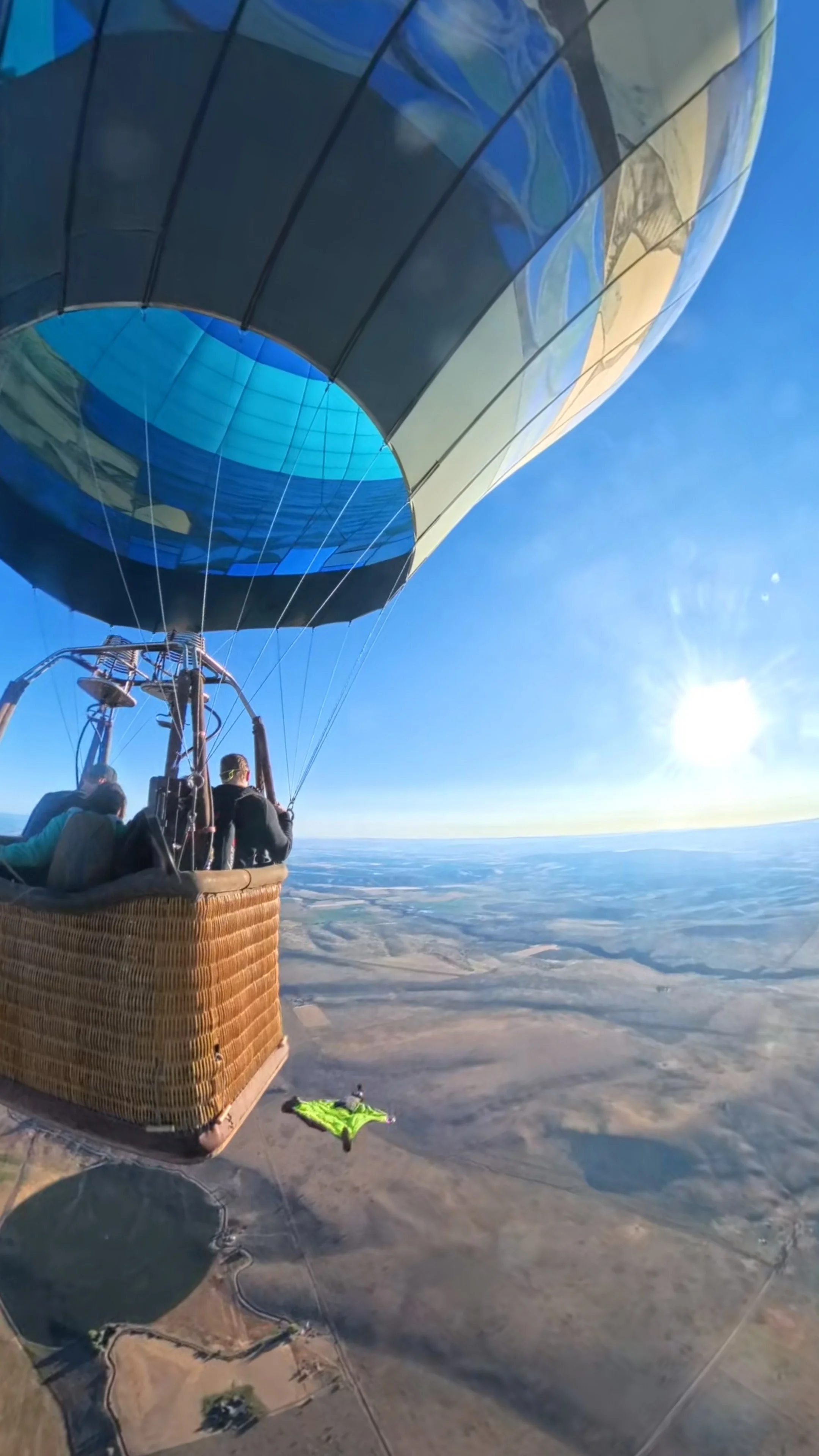 Hot air balloon flying high above a rural landscape on a sunny day with a clear blue sky.