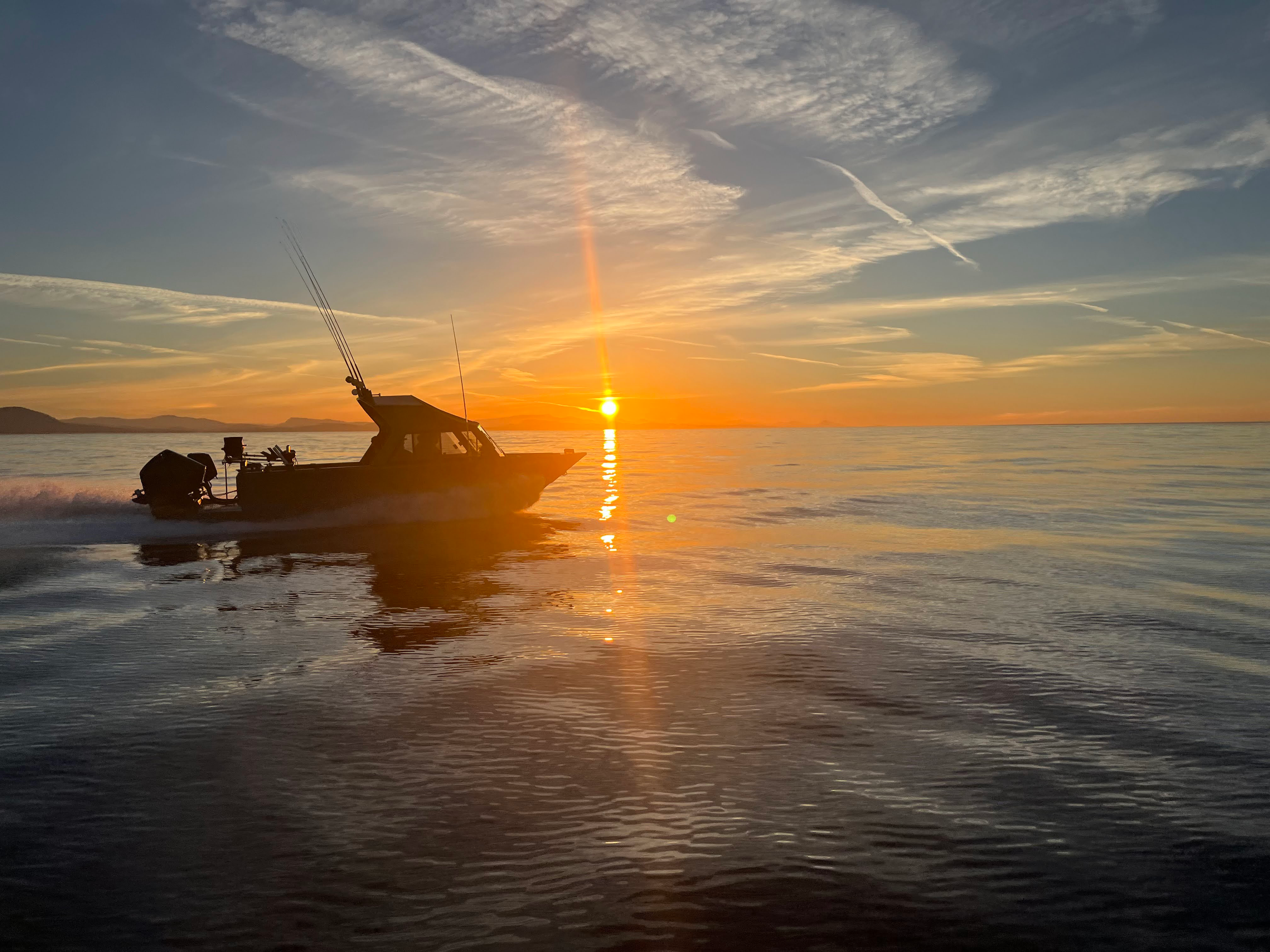 Photograph of a motor boat on a lake. In the background, the sun is setting over a placid lake.