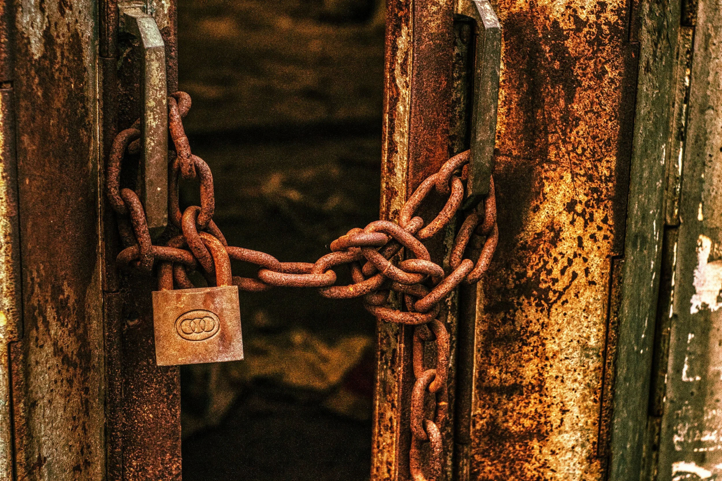 A rusty metal gate secured with a thick chain and padlock, showing signs of age and rust.