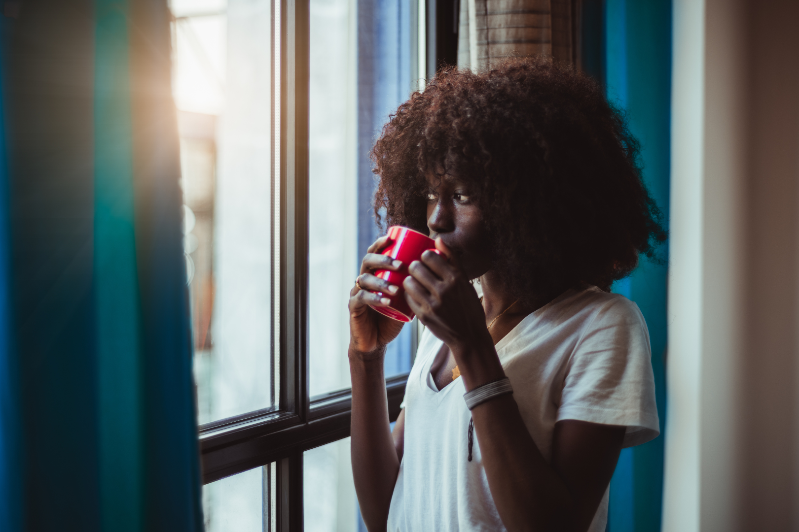black woman looking out the window drinking coffee