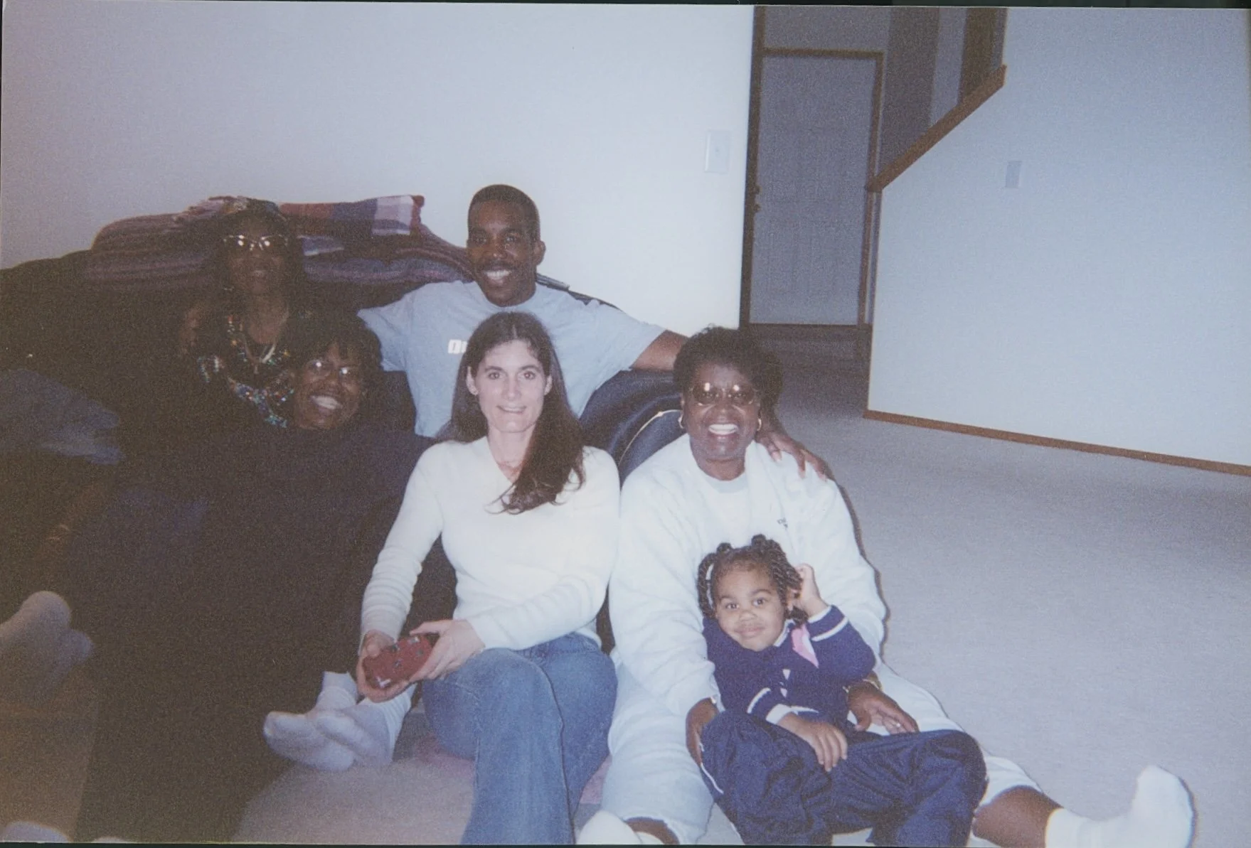 Group of five people, including children, sitting on the floor in a living room, smiling at the camera.